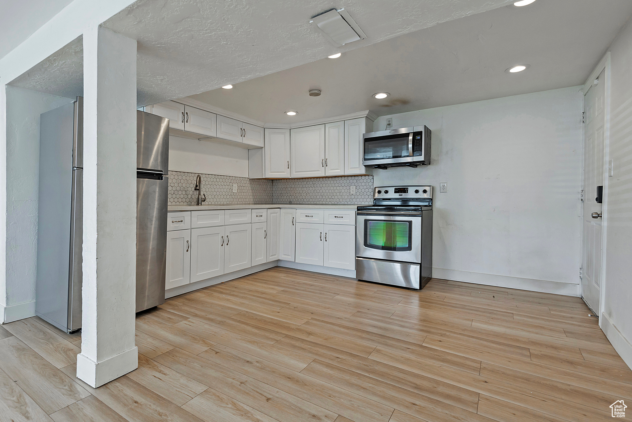 Kitchen featuring light wood finished floors, light countertops, decorative backsplash, stainless steel appliances, and white cabinetry