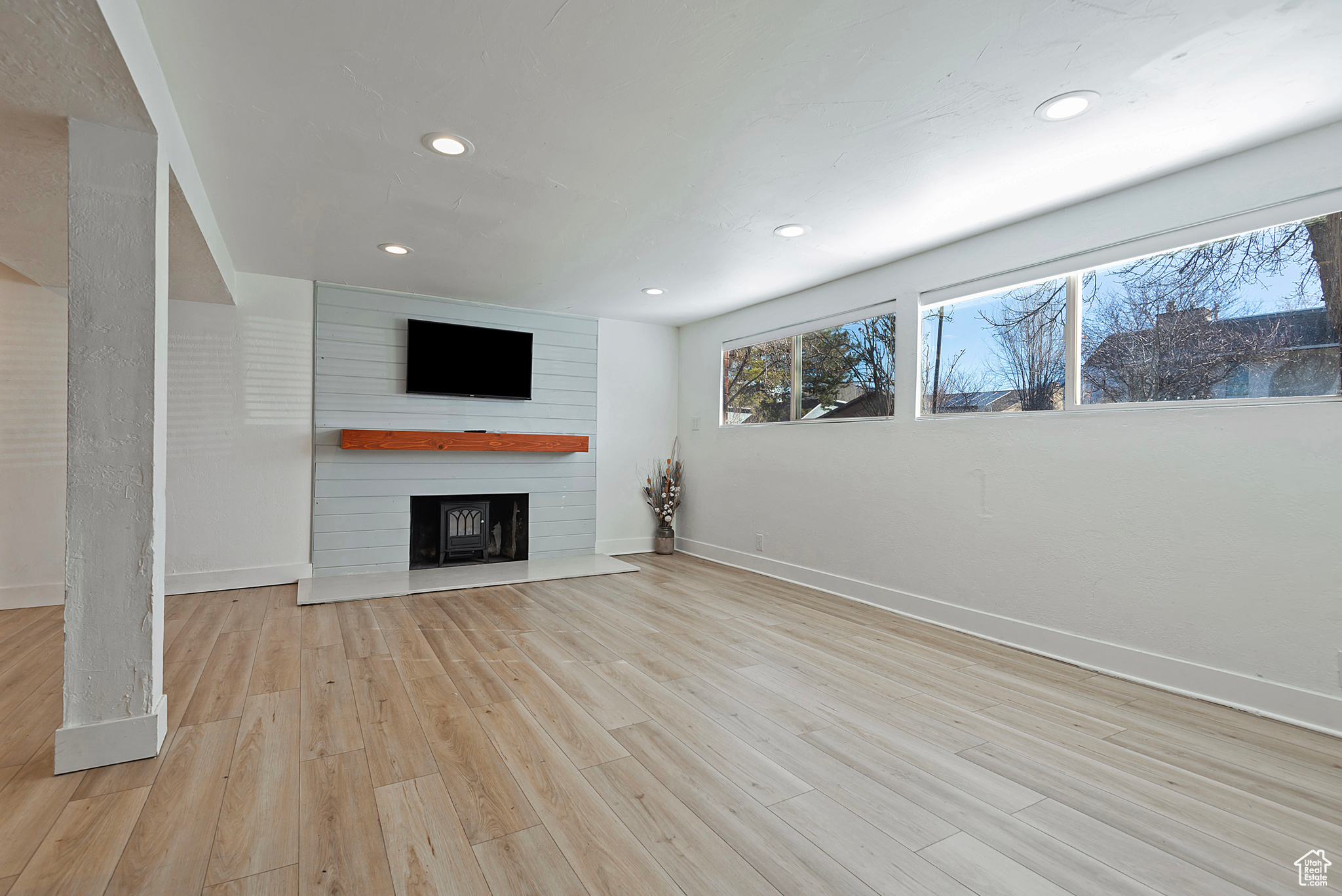 Unfurnished living room featuring recessed lighting, a fireplace, baseboards, and light wood finished floors