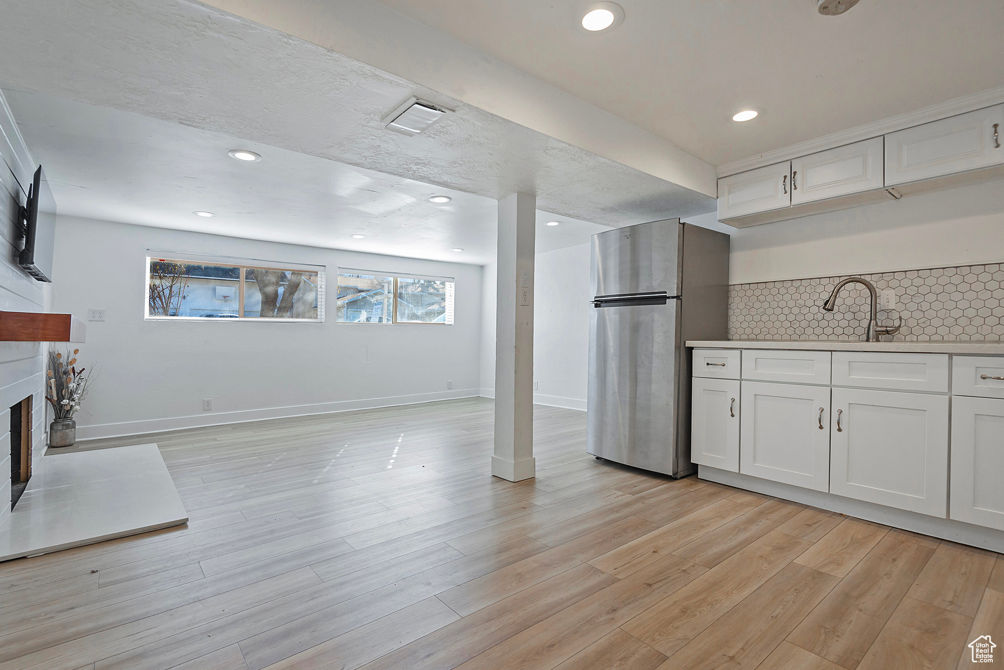 Kitchen featuring a fireplace with raised hearth, freestanding refrigerator, light wood-style floors, white cabinetry, and tasteful backsplash