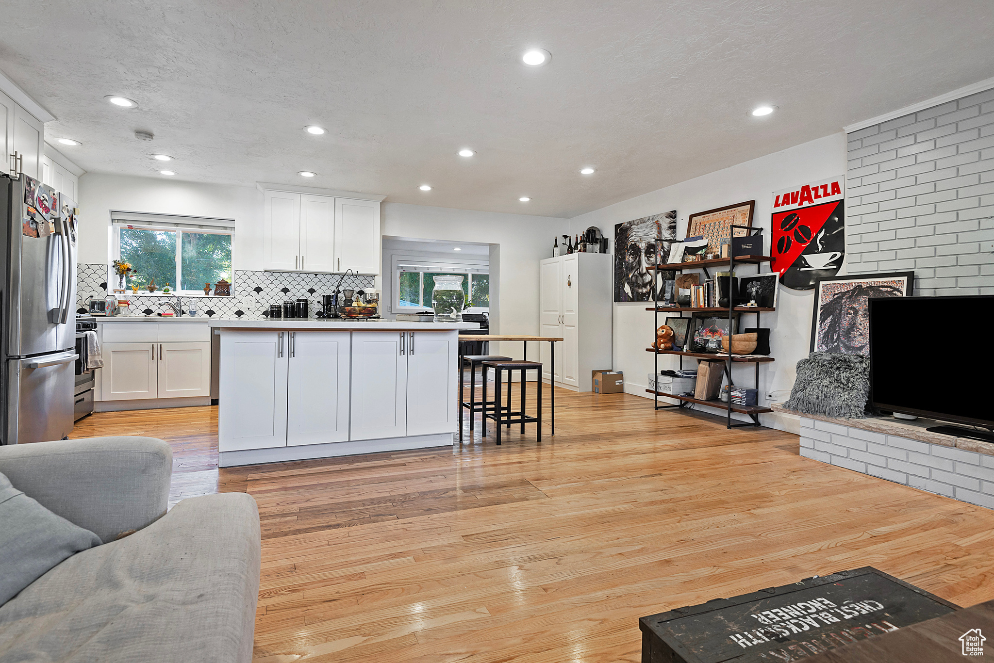 Kitchen with light wood-style flooring, decorative backsplash, appliances with stainless steel finishes, white cabinetry, and open floor plan