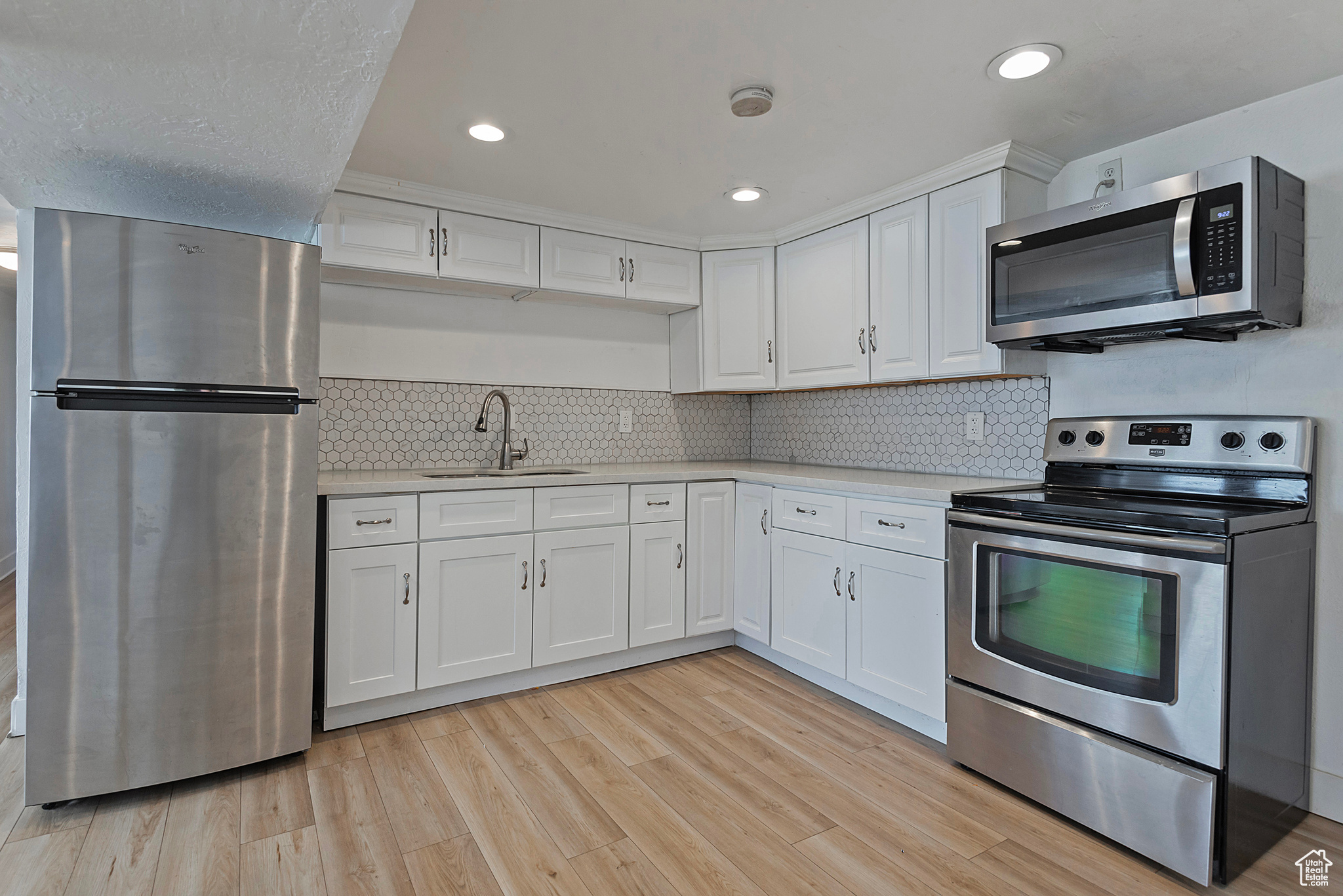 Kitchen featuring light wood-type flooring, light countertops, stainless steel appliances, white cabinetry, and a sink