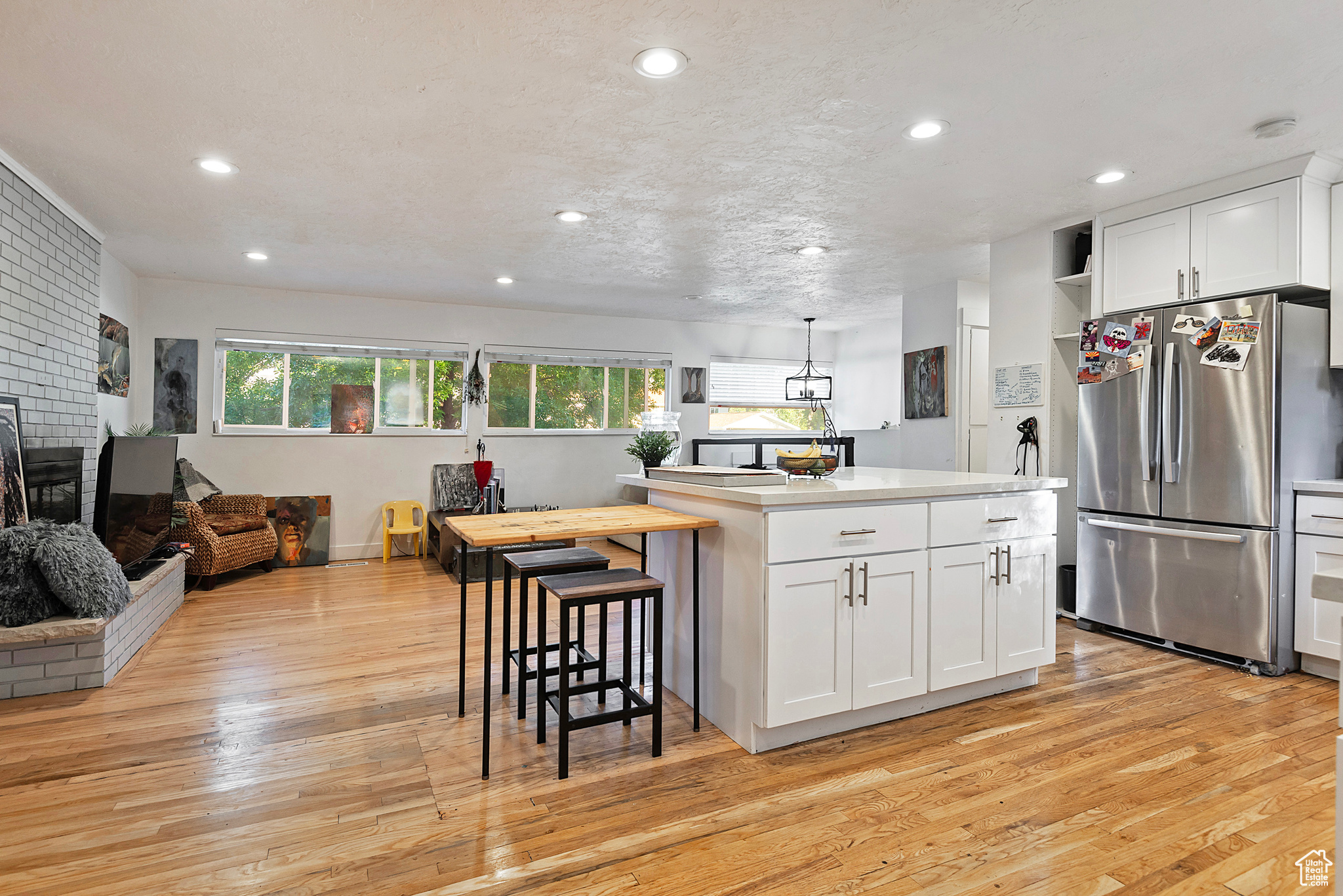 Kitchen featuring light wood finished floors, white cabinets, a brick fireplace, and freestanding refrigerator