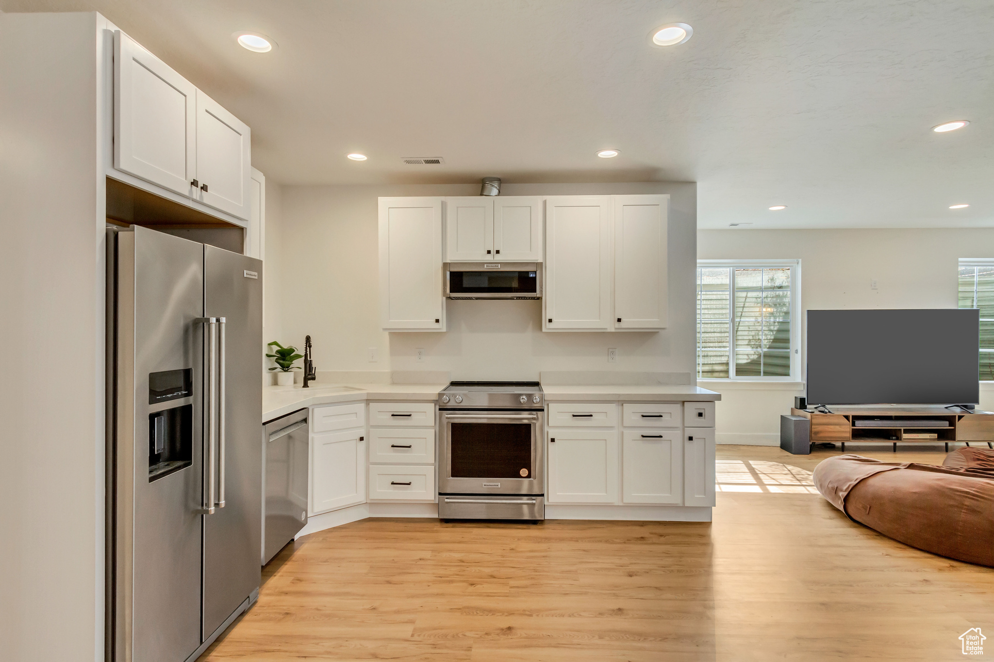 Kitchen with open floor plan, appliances with stainless steel finishes, white cabinetry, and light countertops