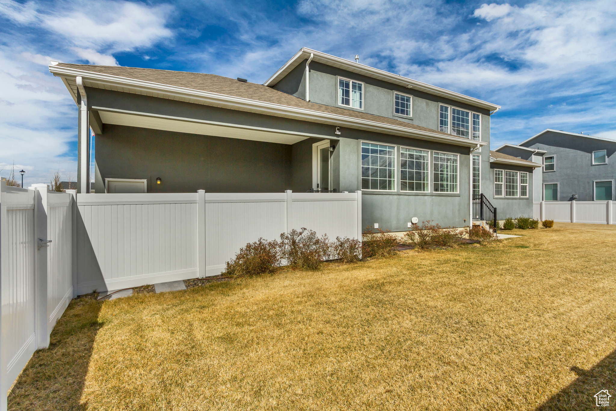 Back of house with stucco siding, a lawn, and fence