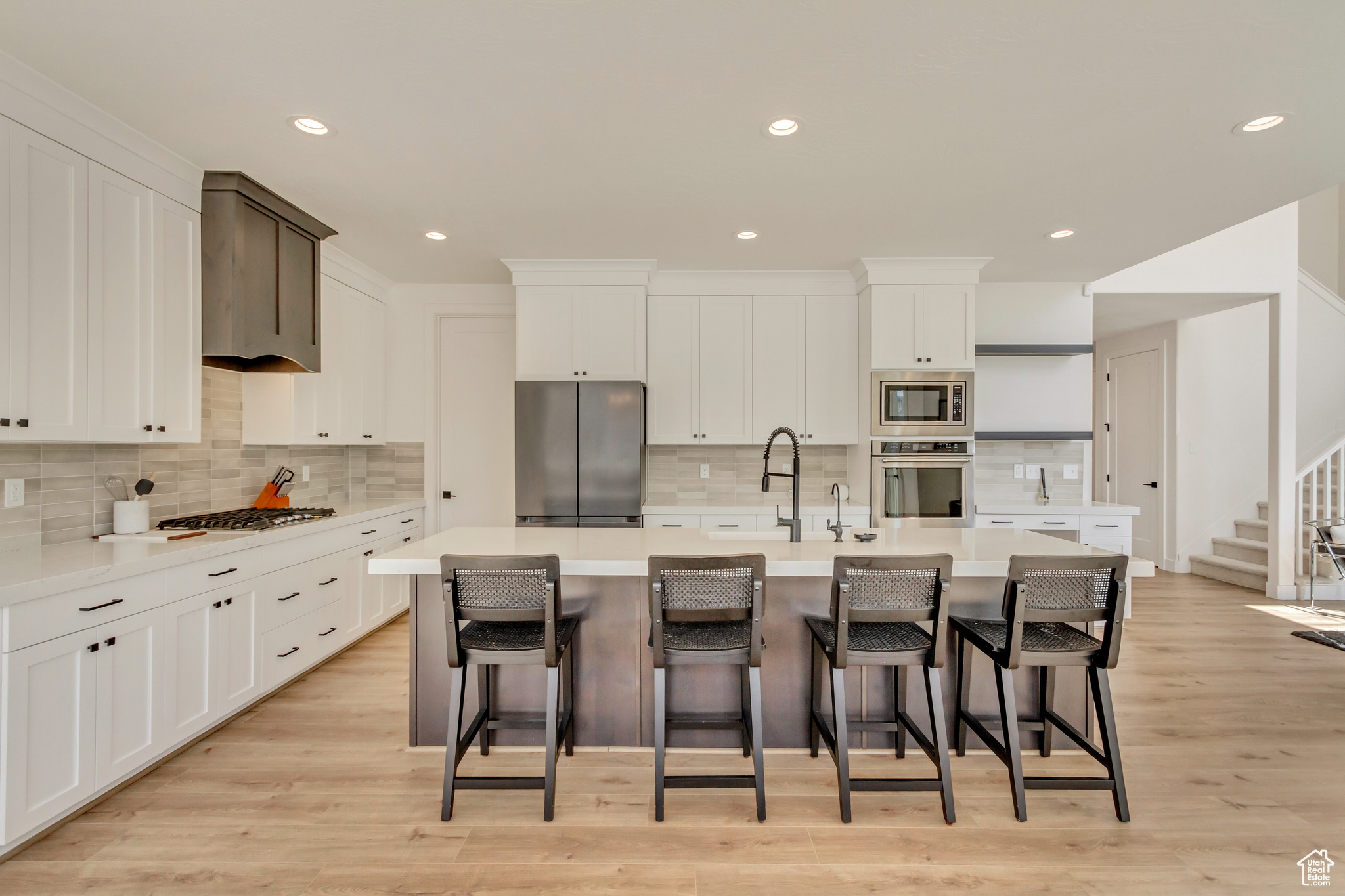 Kitchen with white cabinets, appliances with stainless steel finishes, light wood-style floors, and a kitchen island with sink