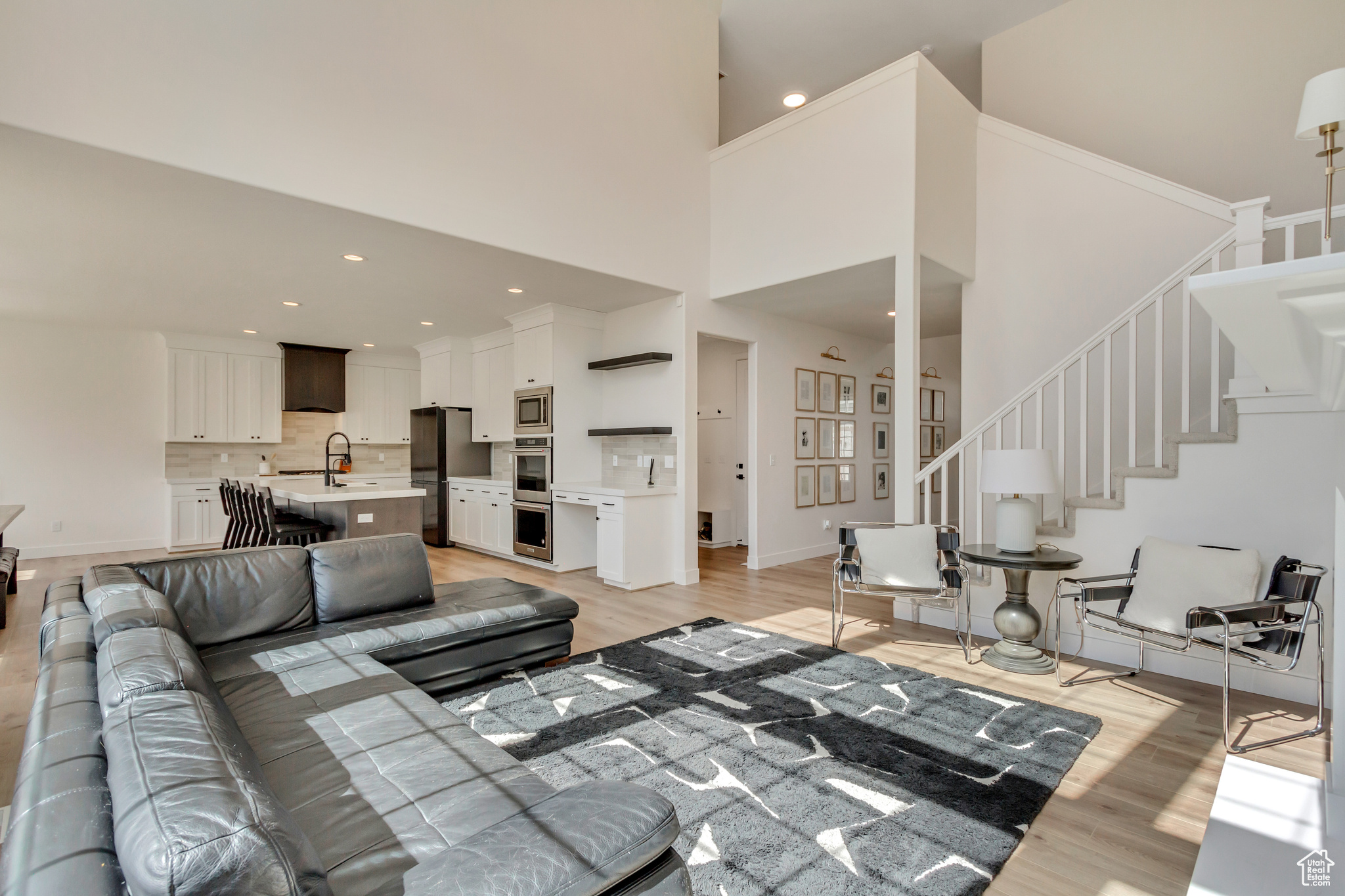 Living area featuring baseboards, stairway, light wood-type flooring, recessed lighting, and a high ceiling