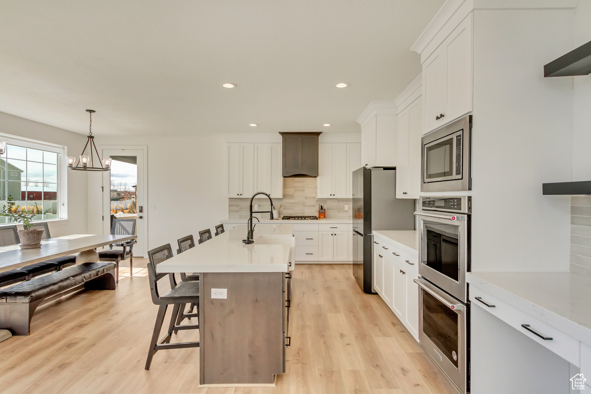 Kitchen featuring decorative backsplash, light wood-style flooring, stainless steel appliances, and light countertops