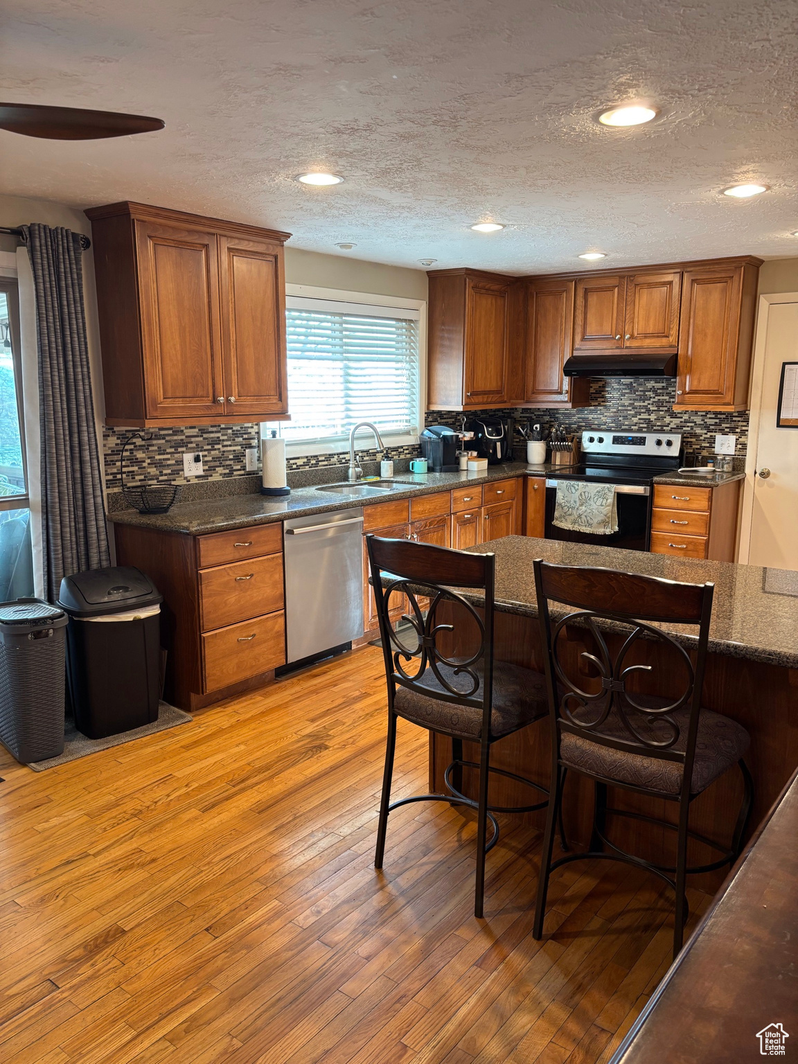 Kitchen with light wood finished floors, under cabinet range hood, a breakfast bar area, stainless steel appliances, and a sink