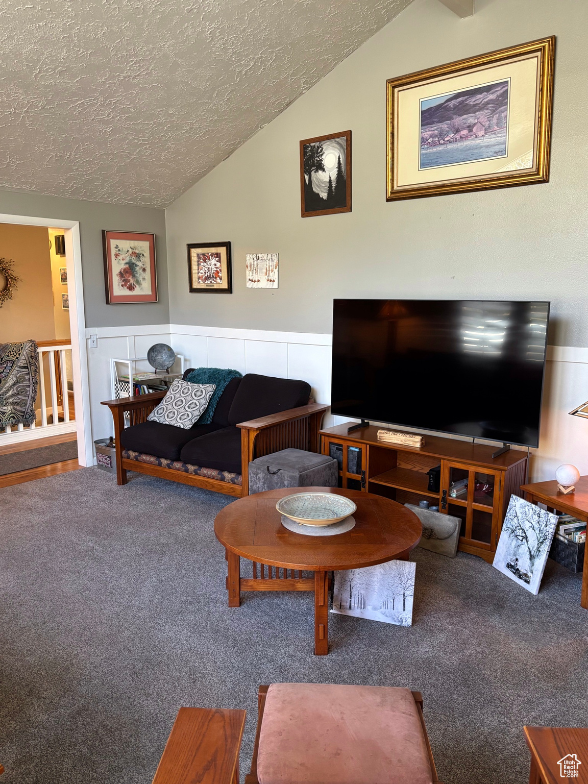 Living area featuring vaulted ceiling, carpet flooring, a wainscoted wall, and a textured ceiling