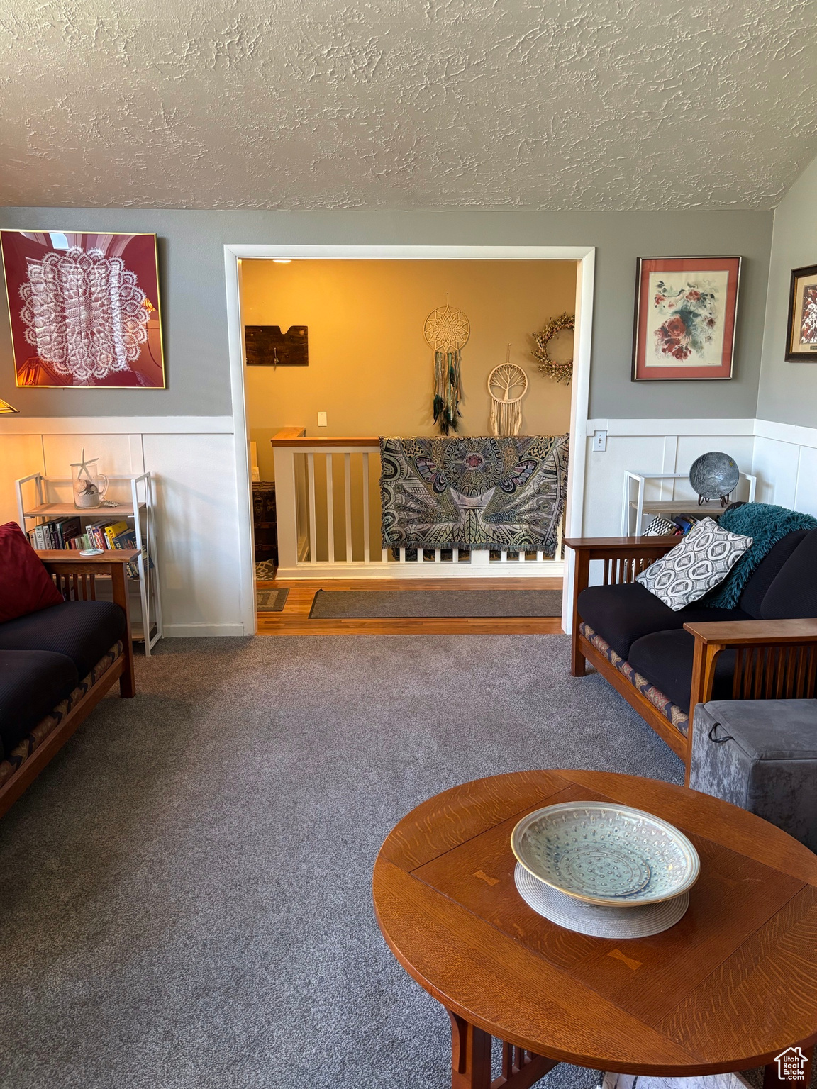 Living area with a wainscoted wall, a textured ceiling, and carpet flooring