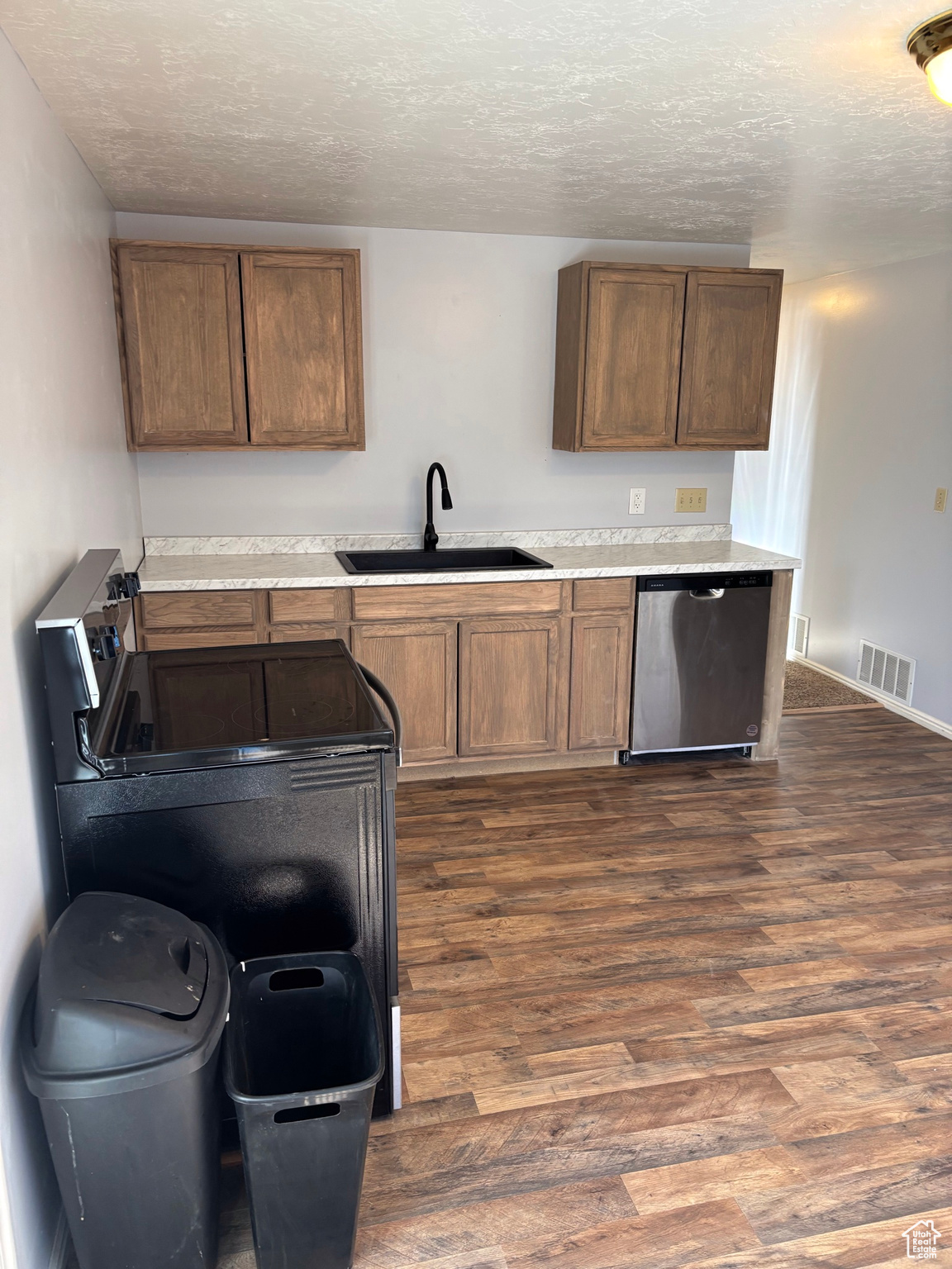 Kitchen featuring visible vents, dark wood-style flooring, a sink, a textured ceiling, and dishwasher