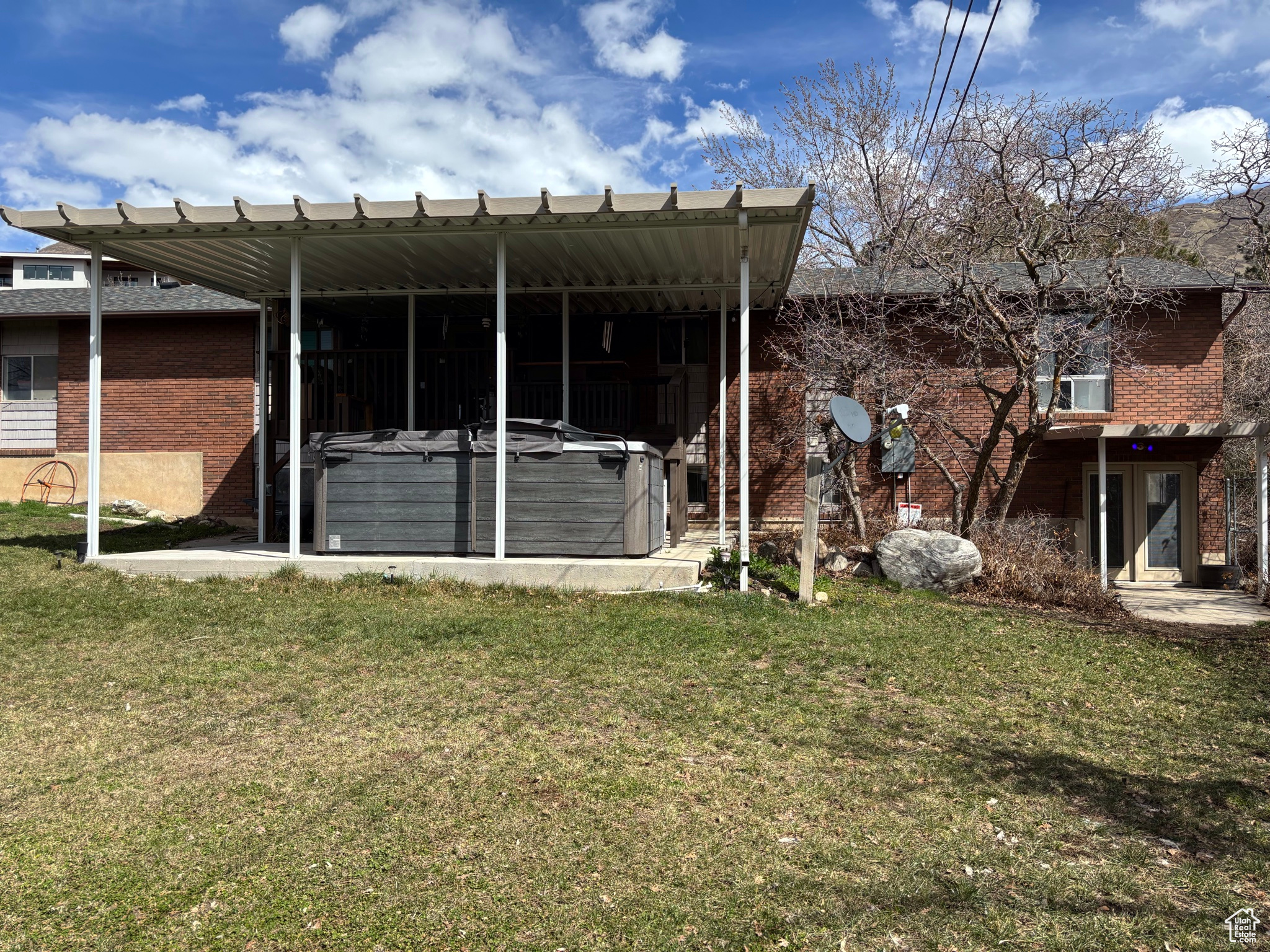 Rear view of property with brick siding, a lawn, and a hot tub