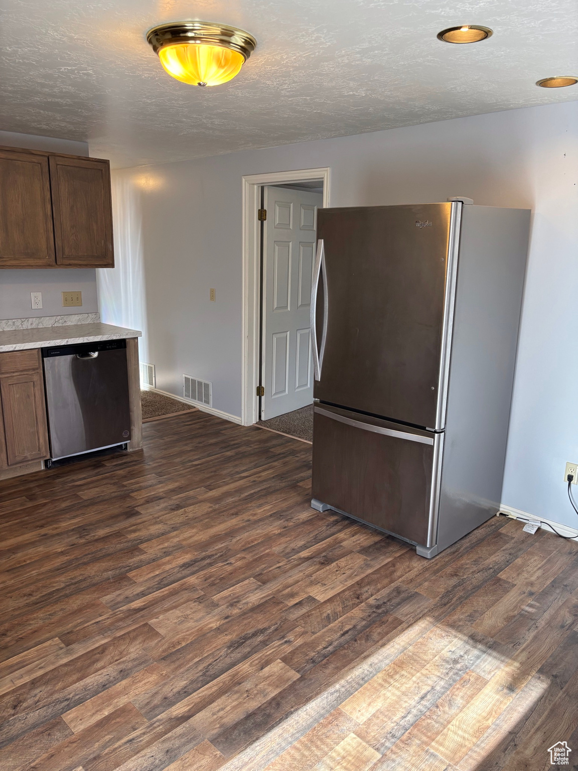 Kitchen featuring visible vents, a textured ceiling, stainless steel appliances, light countertops, and dark wood-style flooring