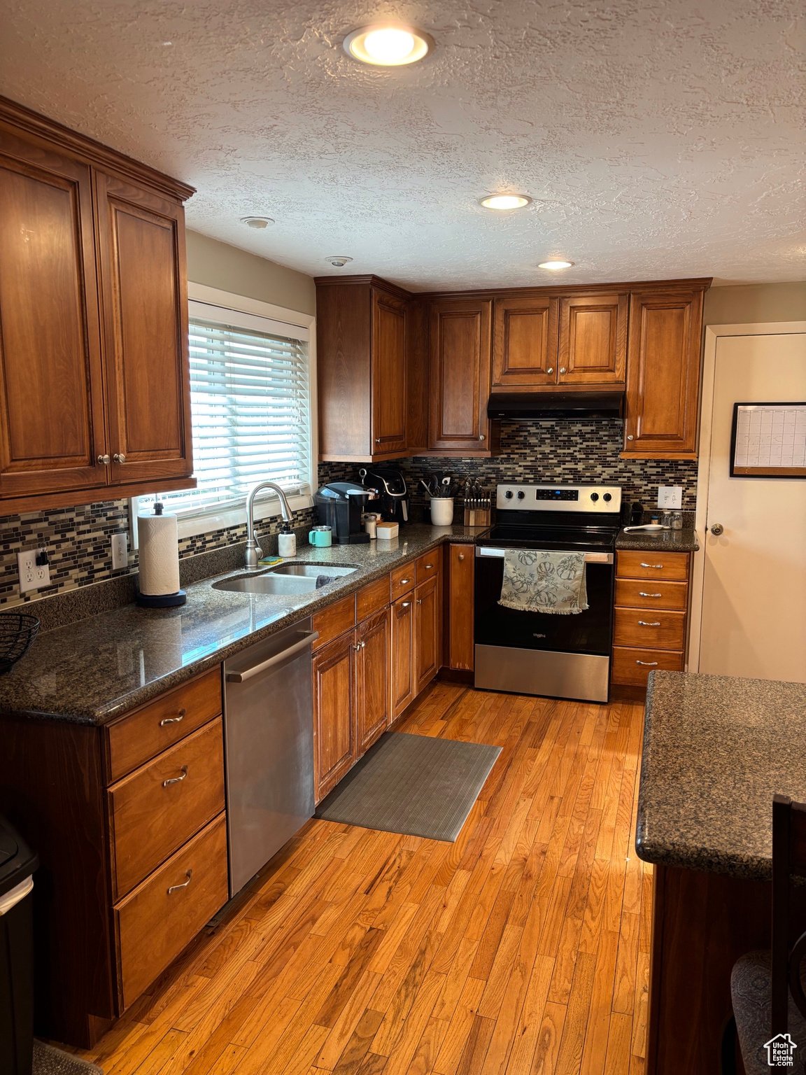 Kitchen featuring a sink, under cabinet range hood, stainless steel appliances, light wood-style floors, and brown cabinetry