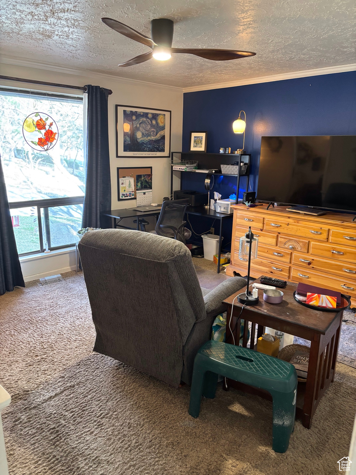 Carpeted living room featuring a textured ceiling, ceiling fan, and ornamental molding