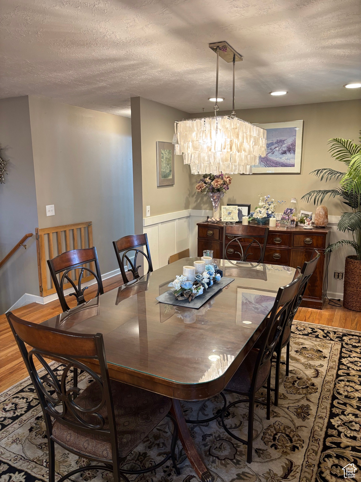 Dining space featuring an inviting chandelier, light wood-style flooring, a wainscoted wall, and a textured ceiling