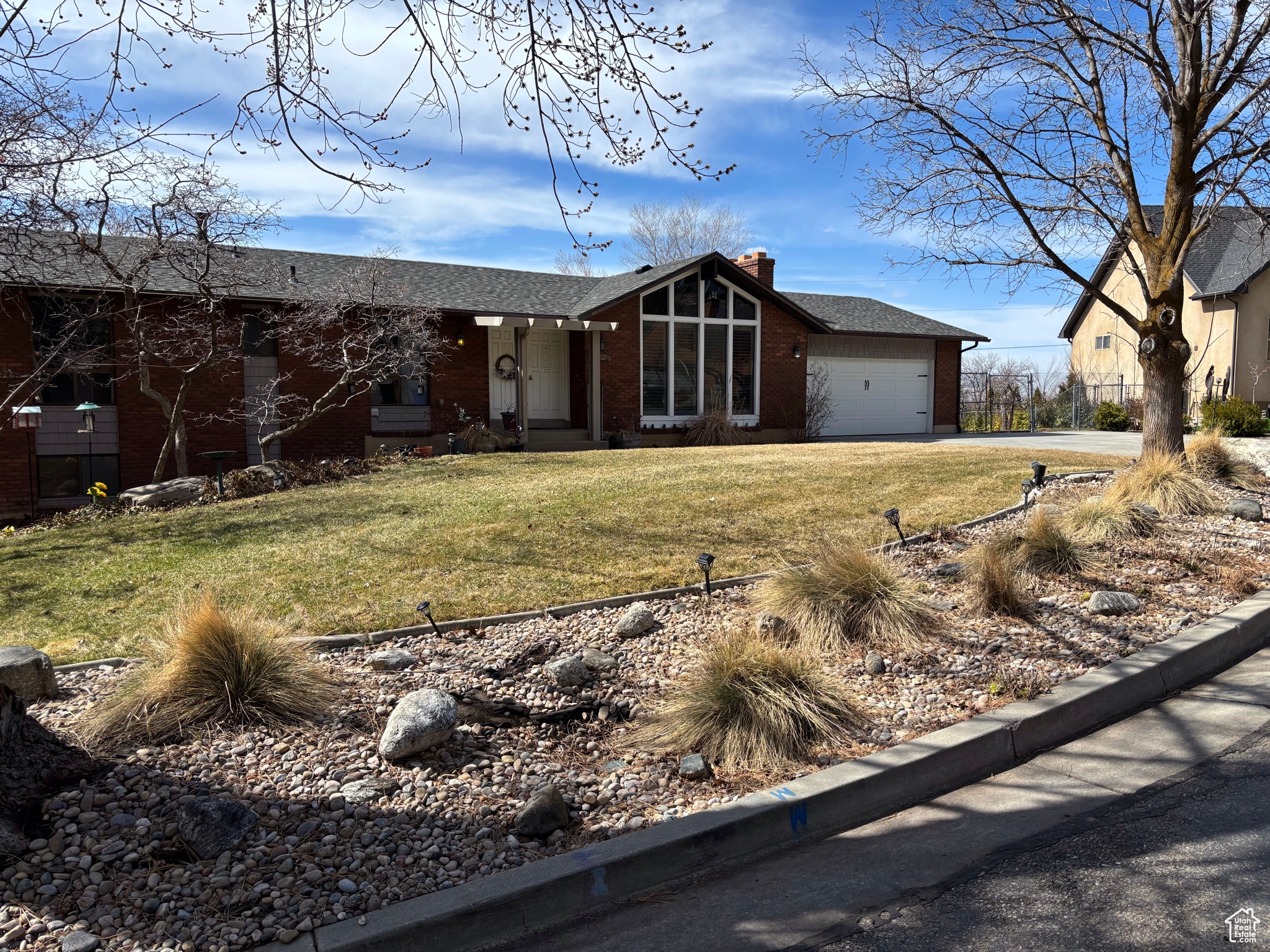 View of front of house featuring driveway, an attached garage, a chimney, a front lawn, and brick siding