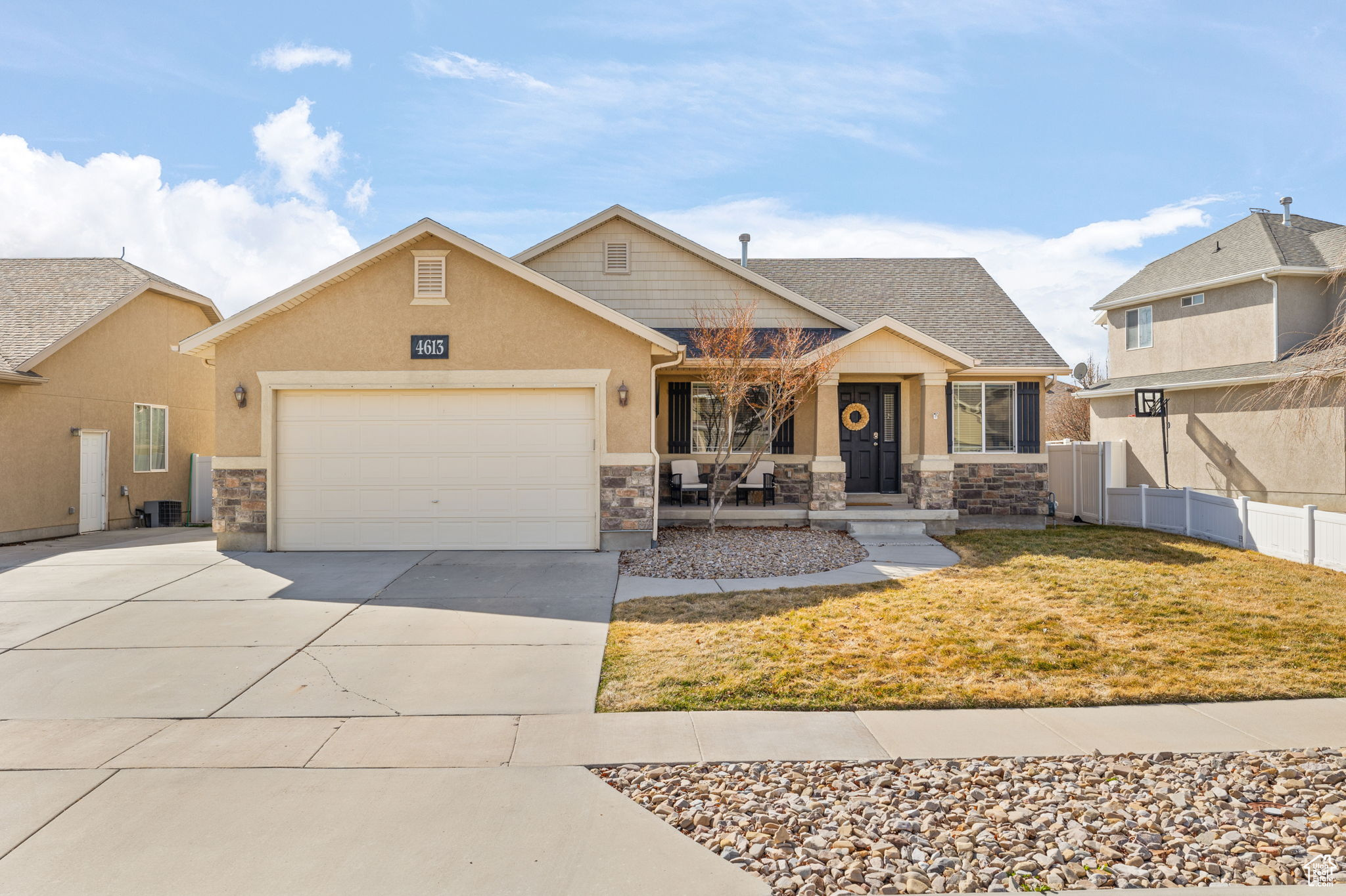 View of front of home featuring an attached garage, fence, stone siding, and driveway