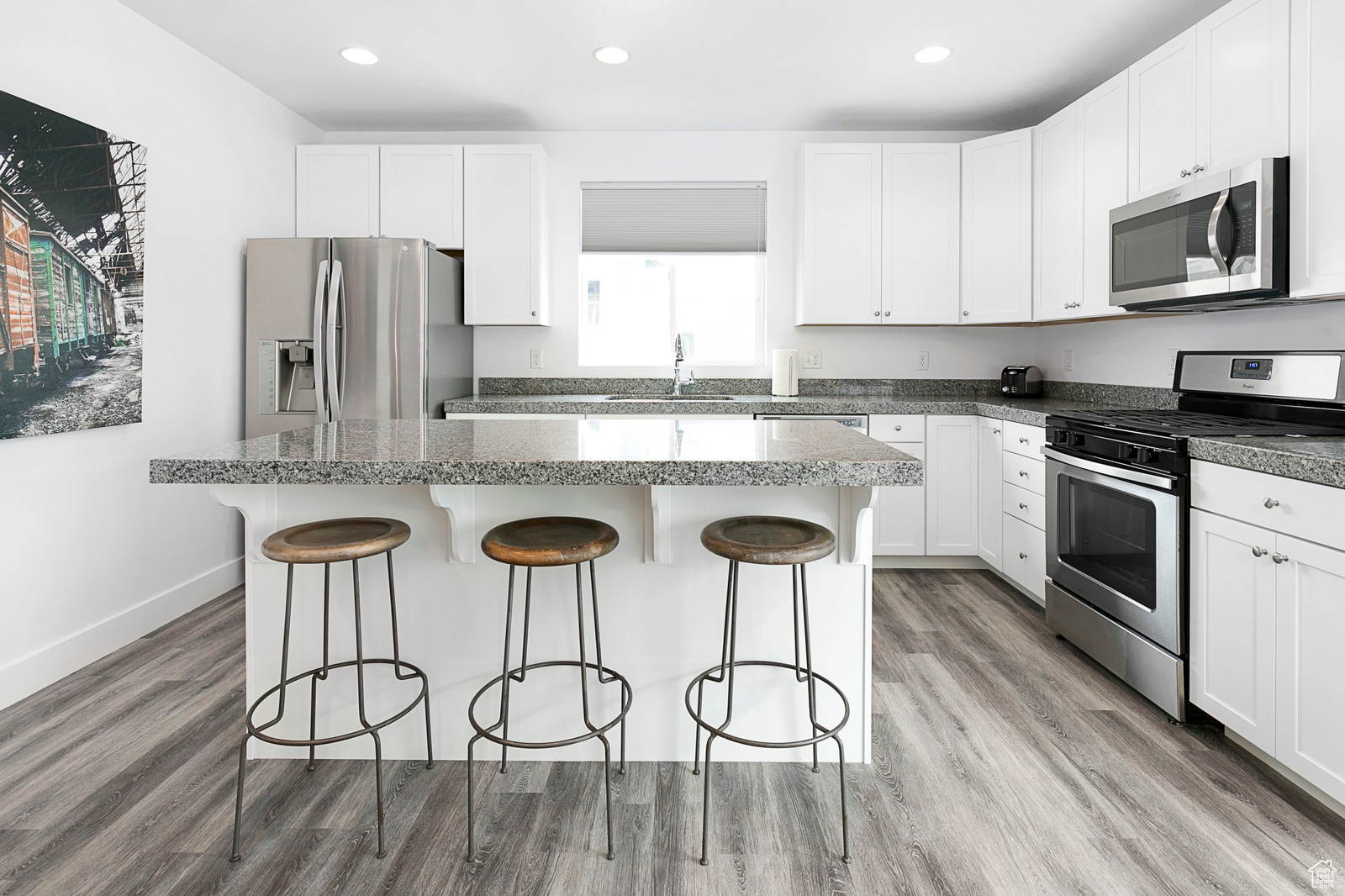 Kitchen with a breakfast bar area, light wood finished floors, a kitchen island, a sink, and appliances with stainless steel finishes