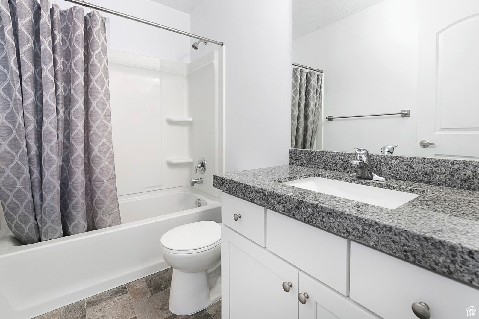 Bathroom featuring vanity, stone tile floors, toilet, and shower / bath combo with shower curtain