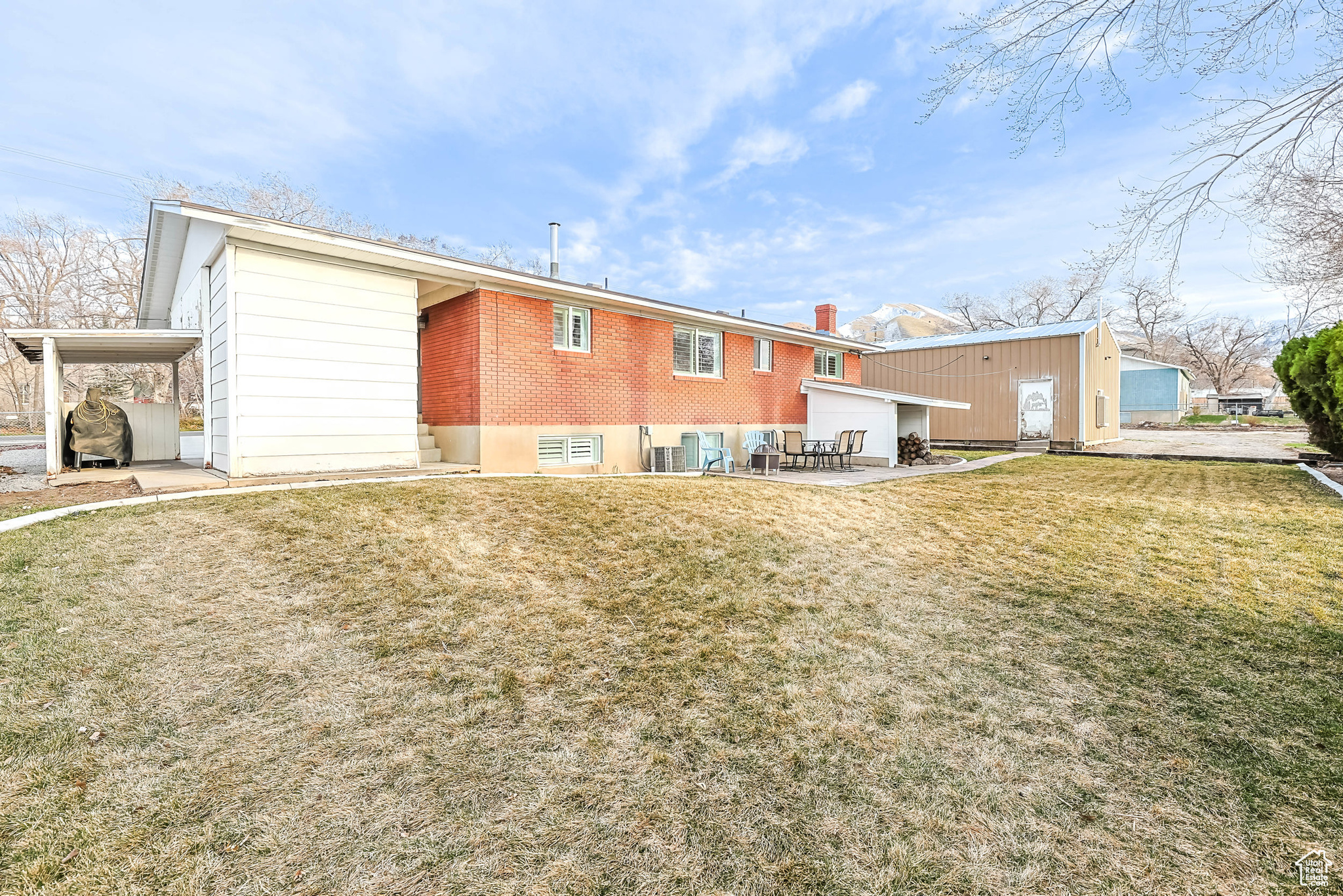 Back of property with an attached carport, brick siding, and a lawn