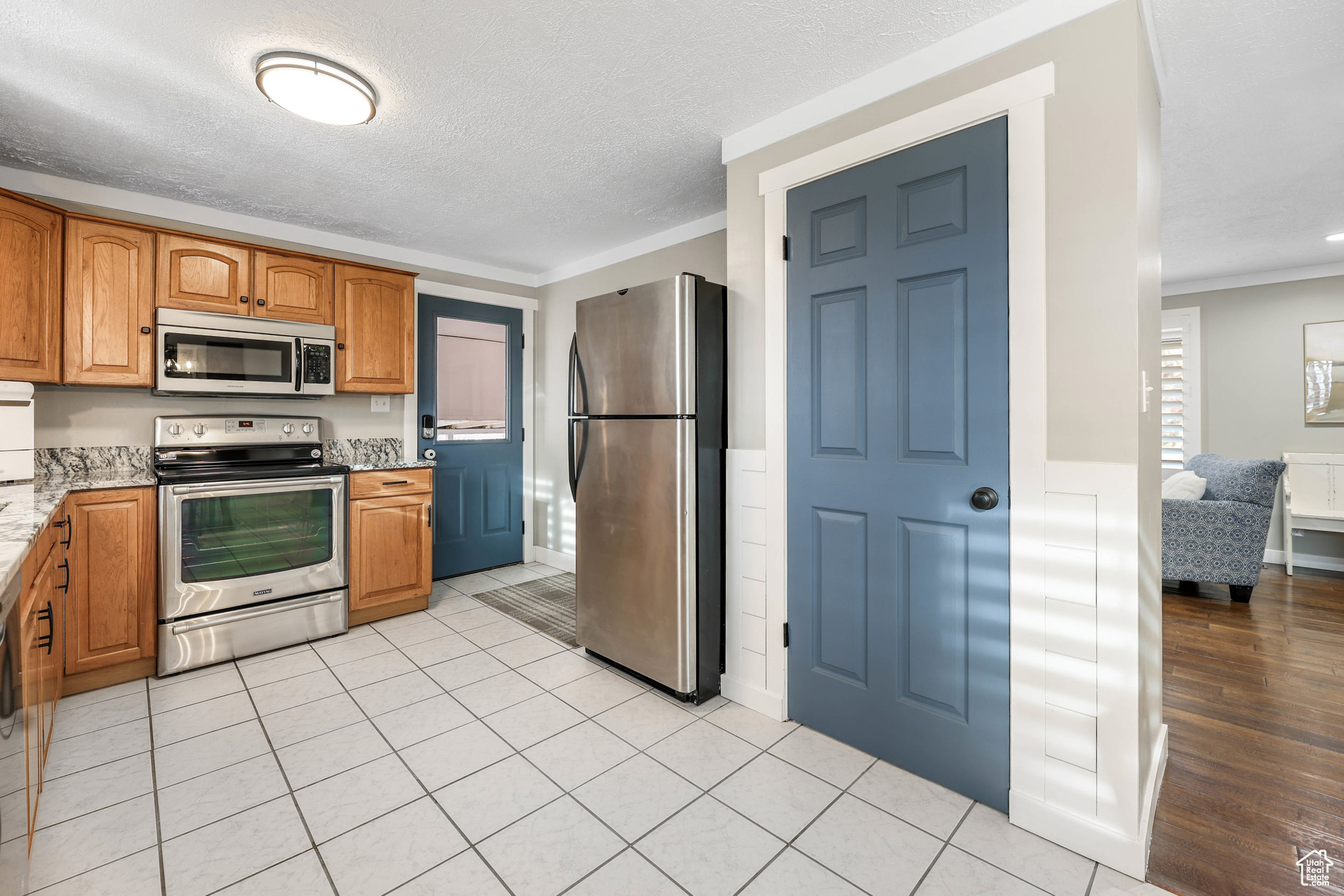 Kitchen featuring light stone countertops, a wainscoted wall, ornamental molding, stainless steel appliances, and a textured ceiling