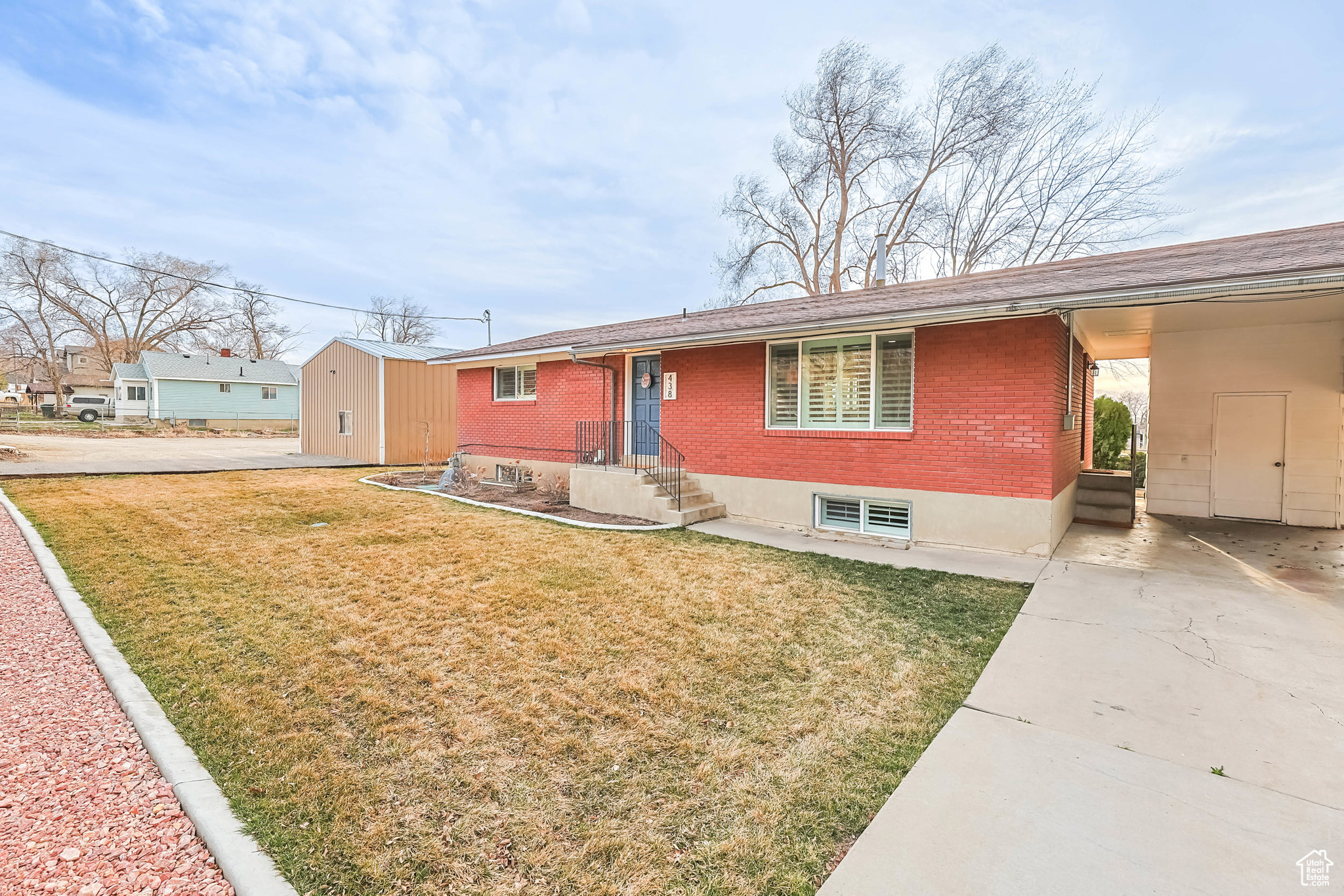 Ranch-style home featuring driveway, a carport, an outdoor structure, a front lawn, and brick siding