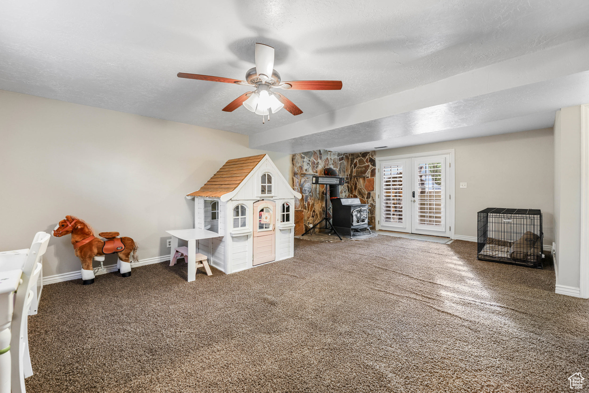 Recreation room featuring a ceiling fan, a textured ceiling, carpet floors, baseboards, and a wood stove