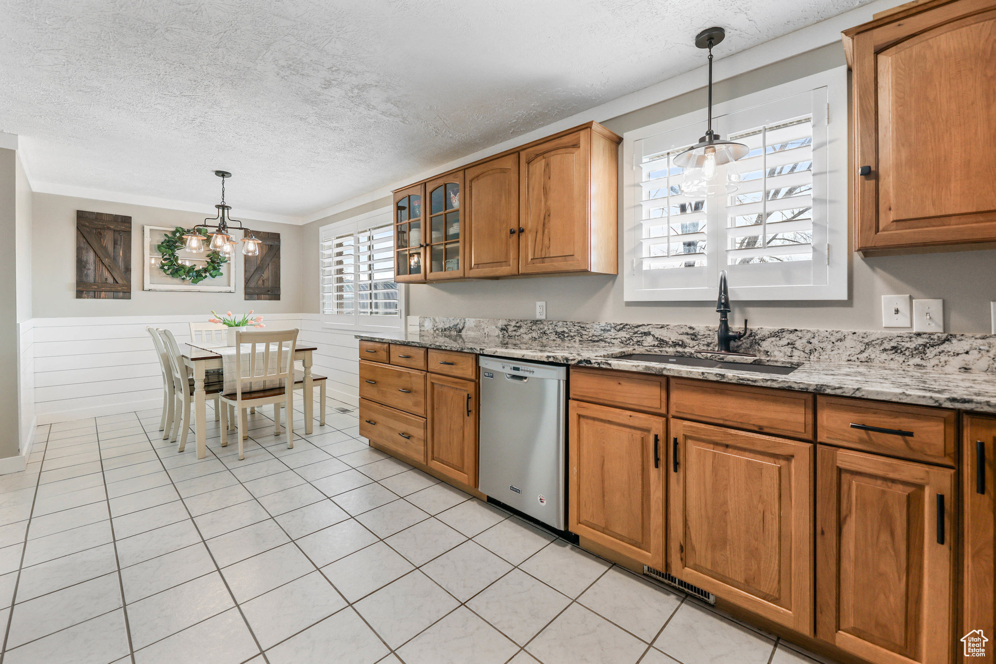 Kitchen featuring light stone counters, brown cabinets, dishwasher, and a sink