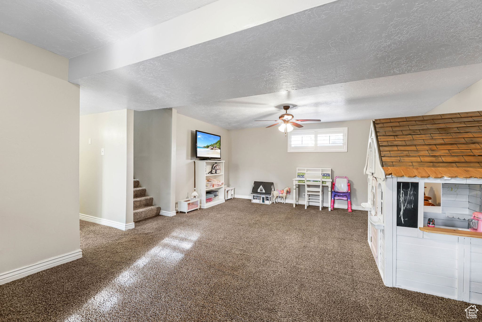 Unfurnished living room with a ceiling fan, a textured ceiling, carpet floors, baseboards, and stairs