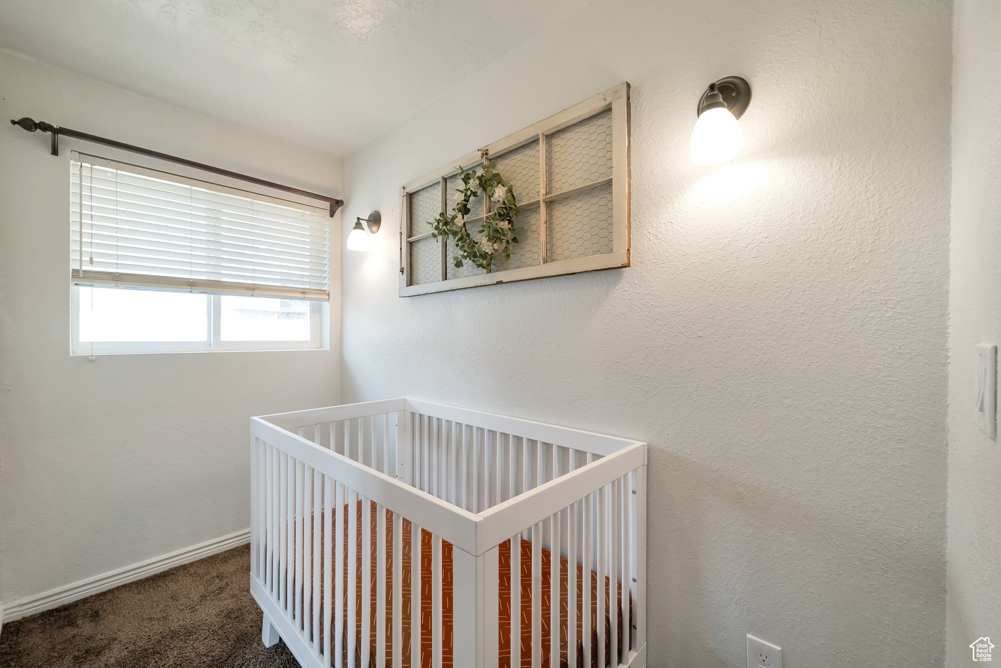 Bedroom featuring a textured wall, baseboards, a nursery area, and carpet floors