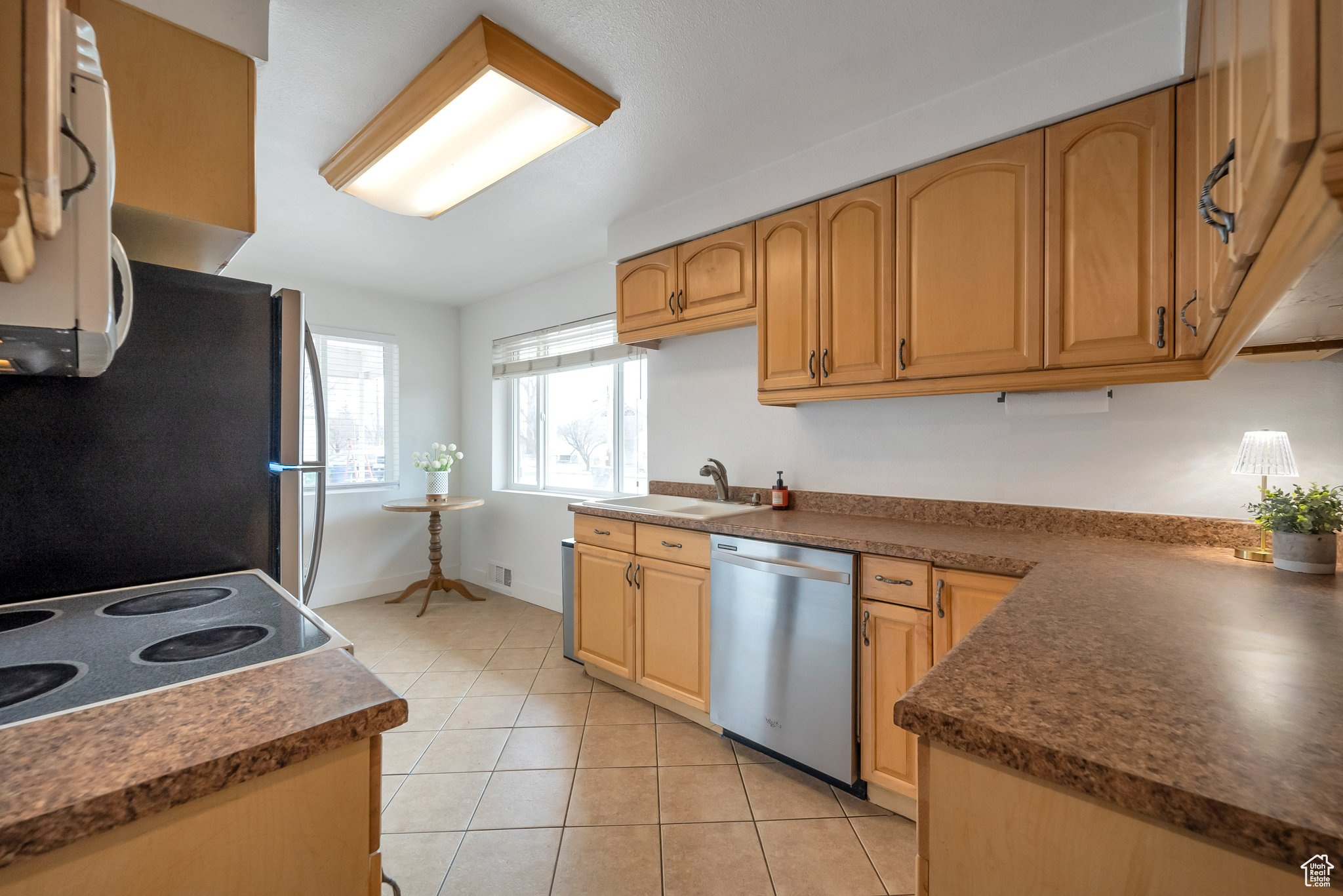 Kitchen with a sink, dark countertops, appliances with stainless steel finishes, and light tile patterned floors