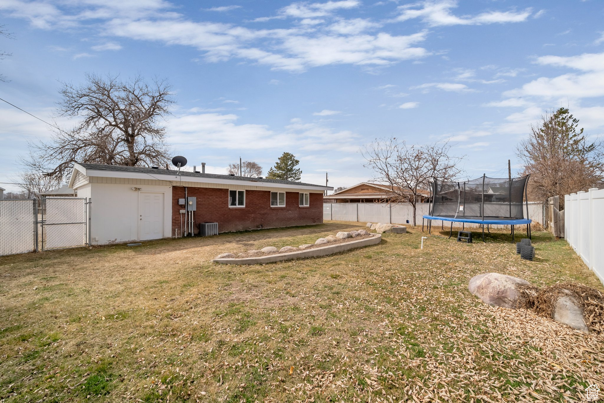 View of yard with a trampoline, central AC, a fenced backyard, and a gate