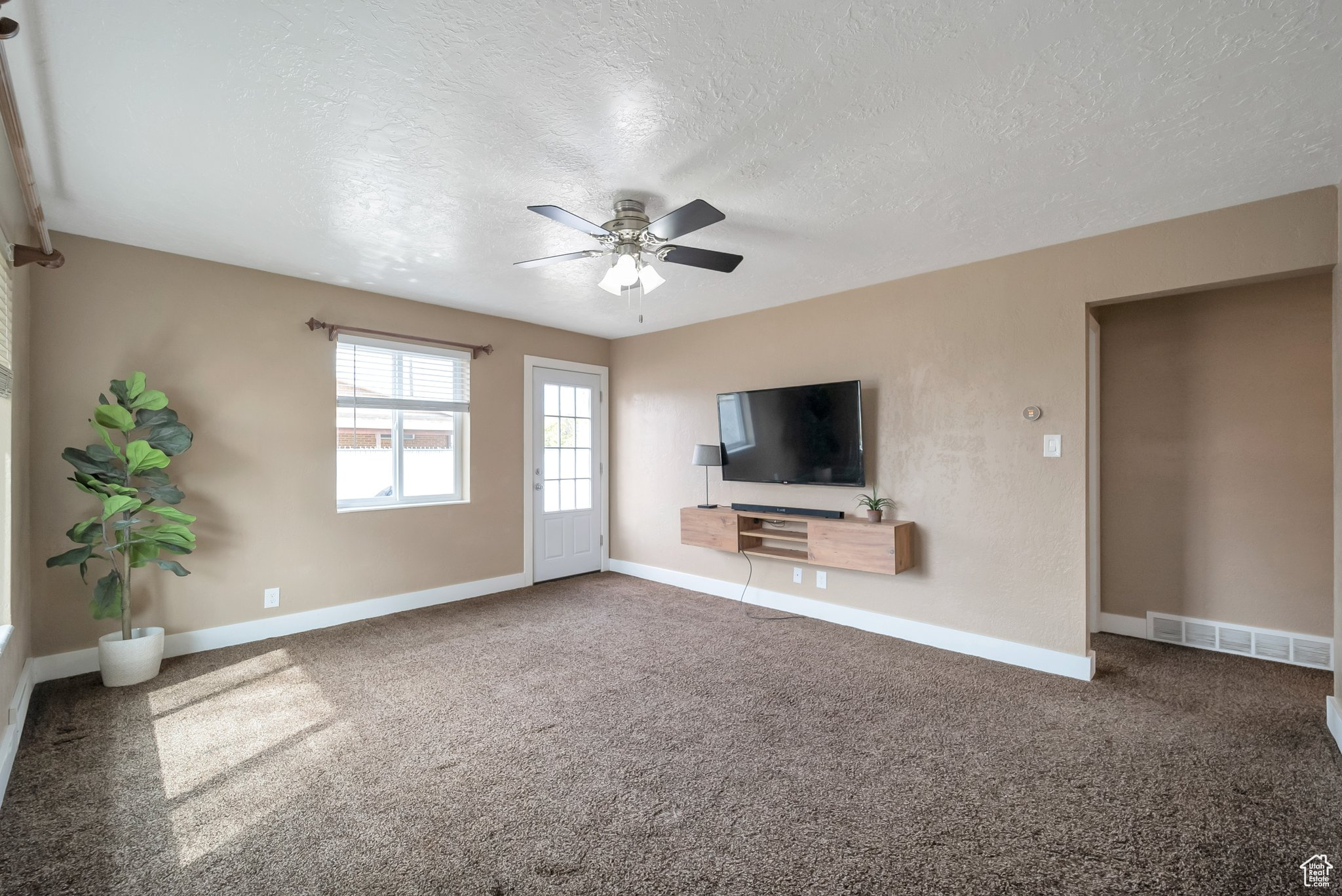 Unfurnished living room featuring visible vents, a ceiling fan, carpet flooring, and a textured ceiling