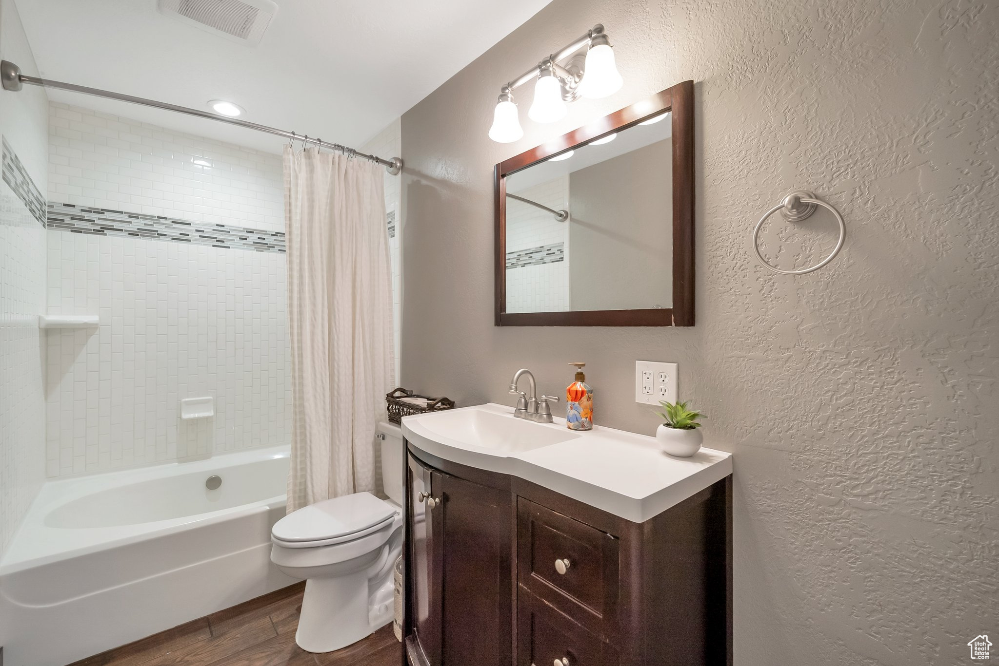 Bathroom with visible vents, toilet, wood finished floors, shower / bath combination with curtain, and a textured wall