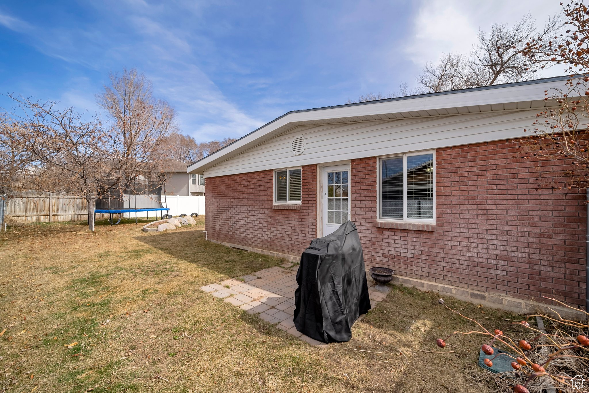 Rear view of property with brick siding, a lawn, a trampoline, and fence