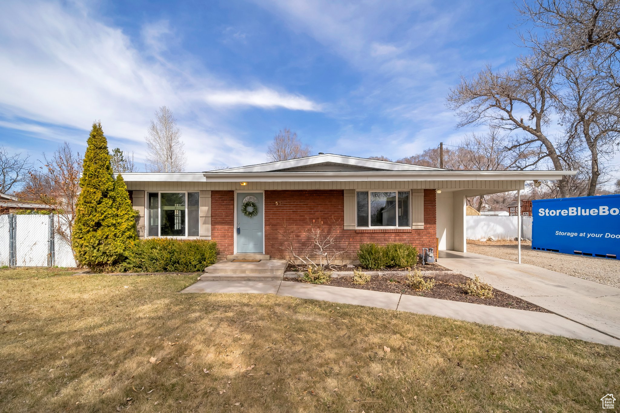 View of front of property featuring an attached carport, a front yard, fence, concrete driveway, and brick siding