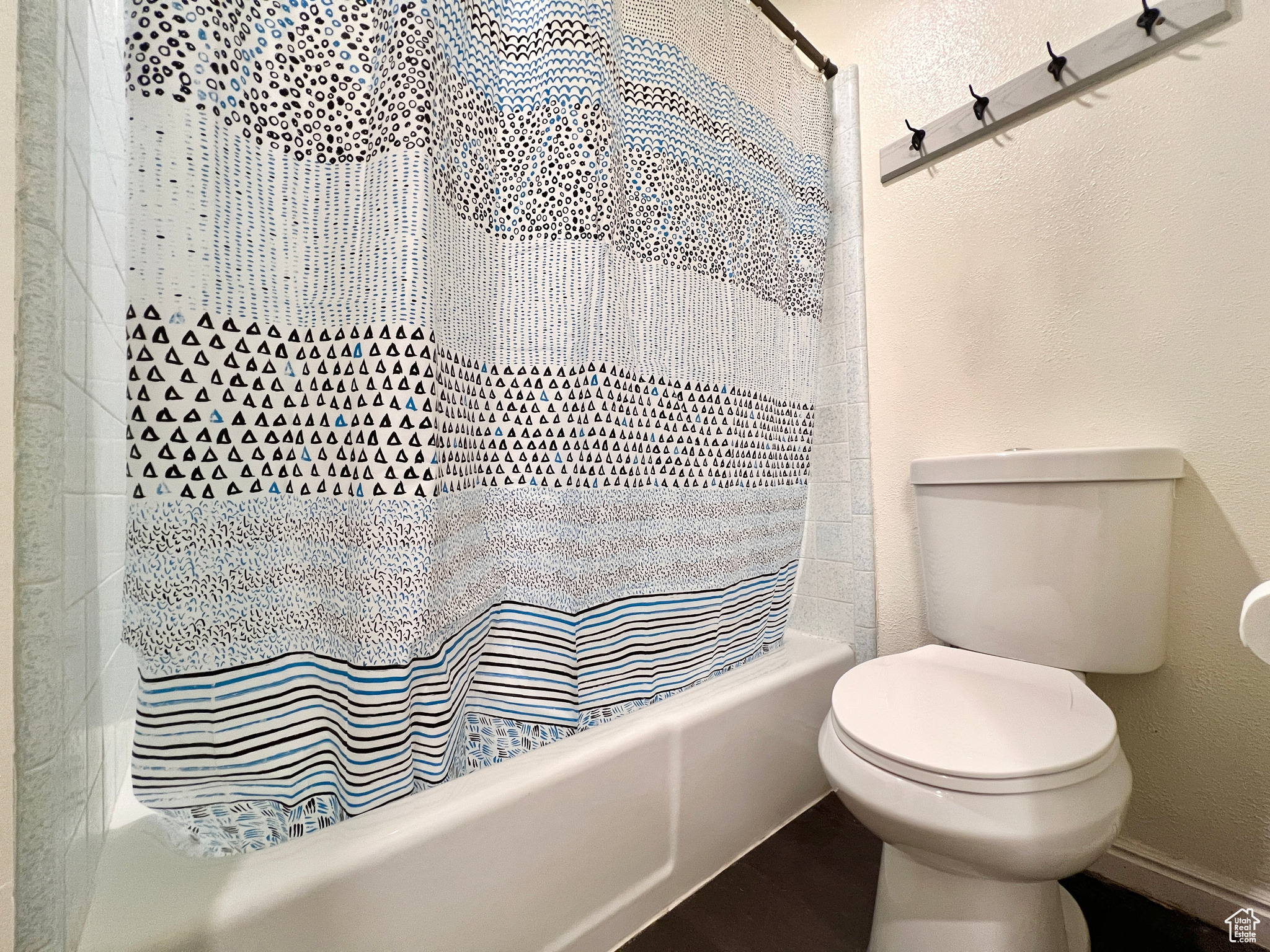 Full bathroom featuring shower / bath combo with shower curtain, toilet, and a textured wall