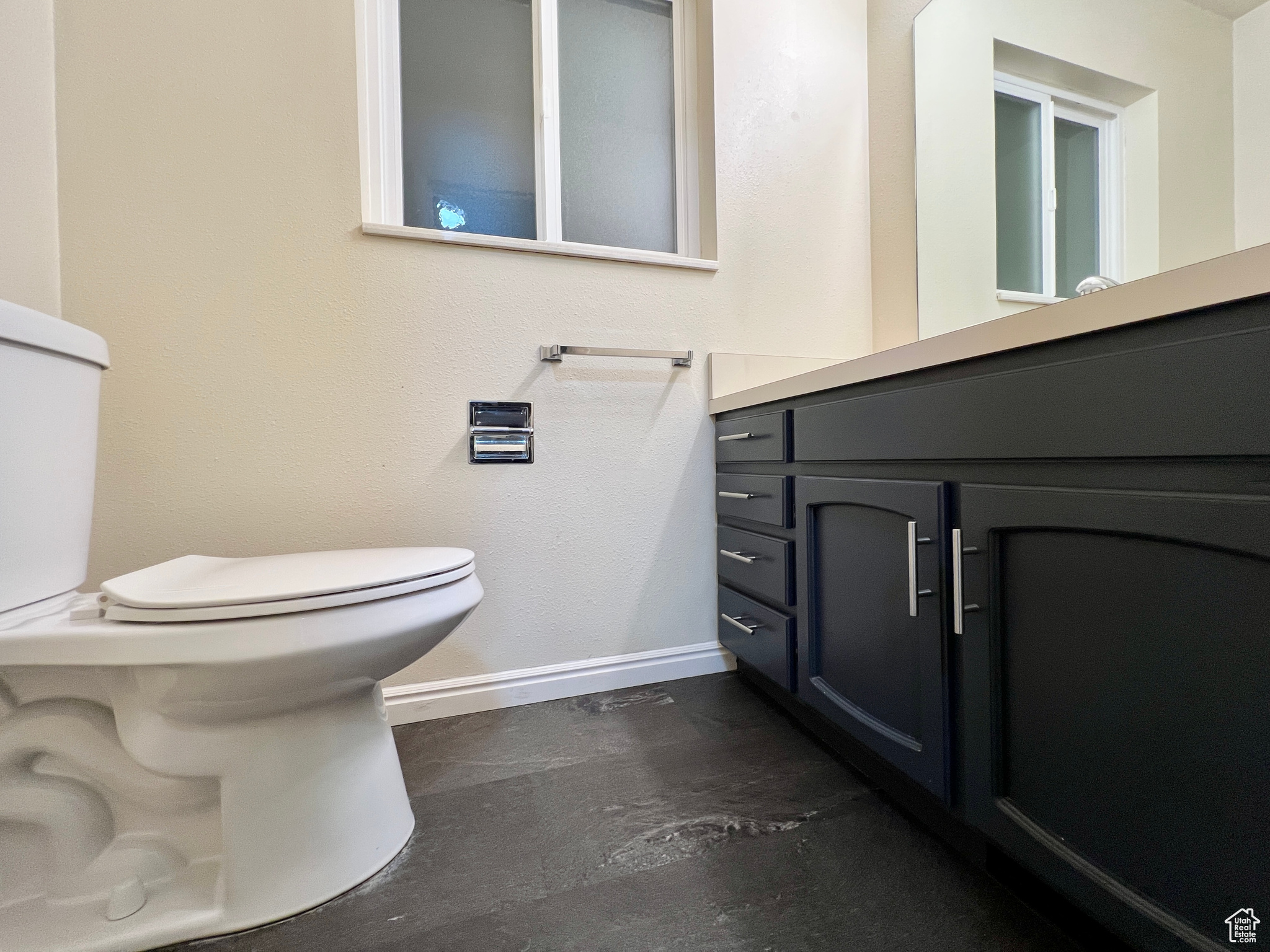 Bathroom with concrete flooring, toilet, vanity, and baseboards