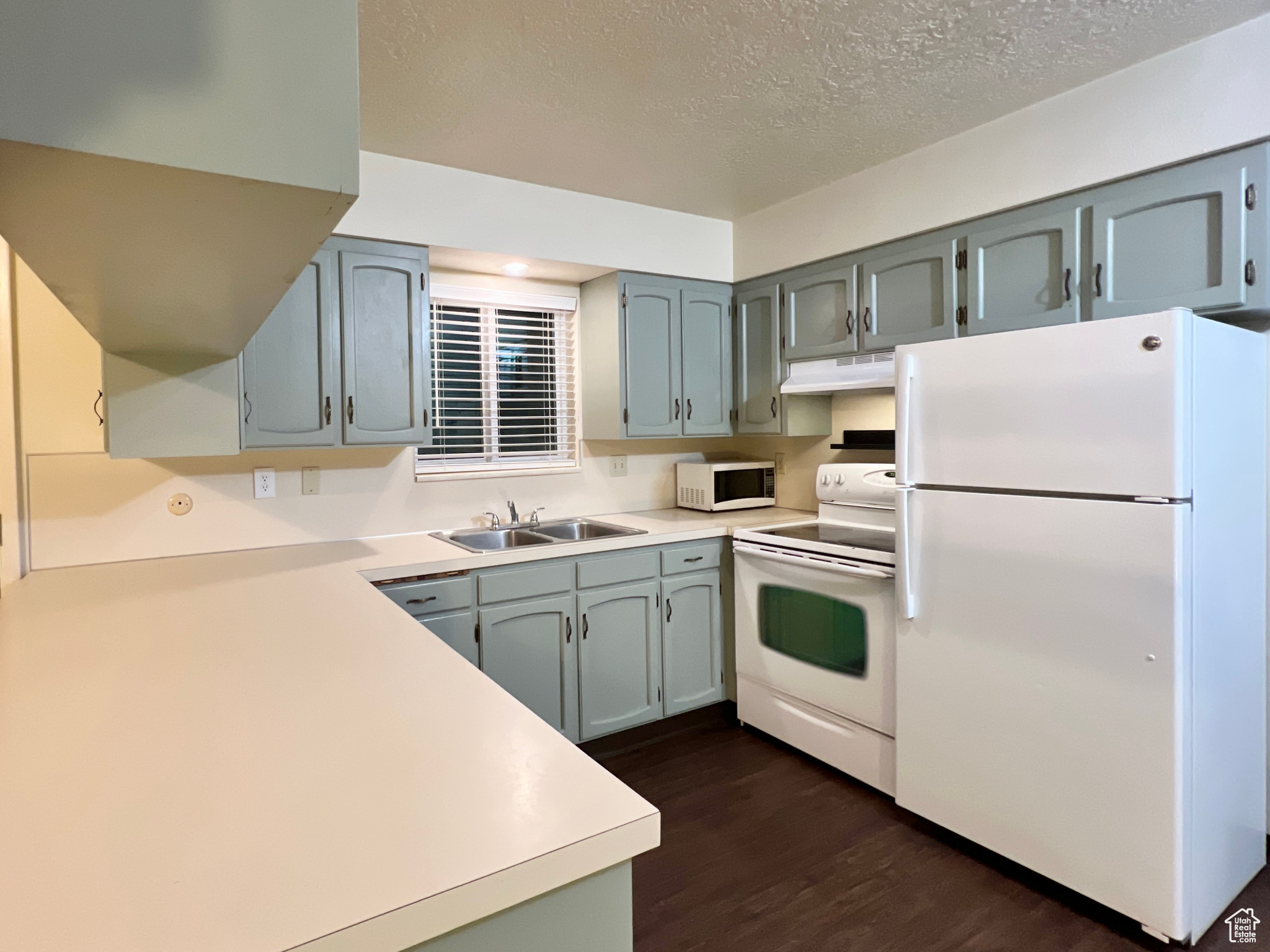 Kitchen featuring white appliances, a sink, dark wood-type flooring, under cabinet range hood, and a textured ceiling