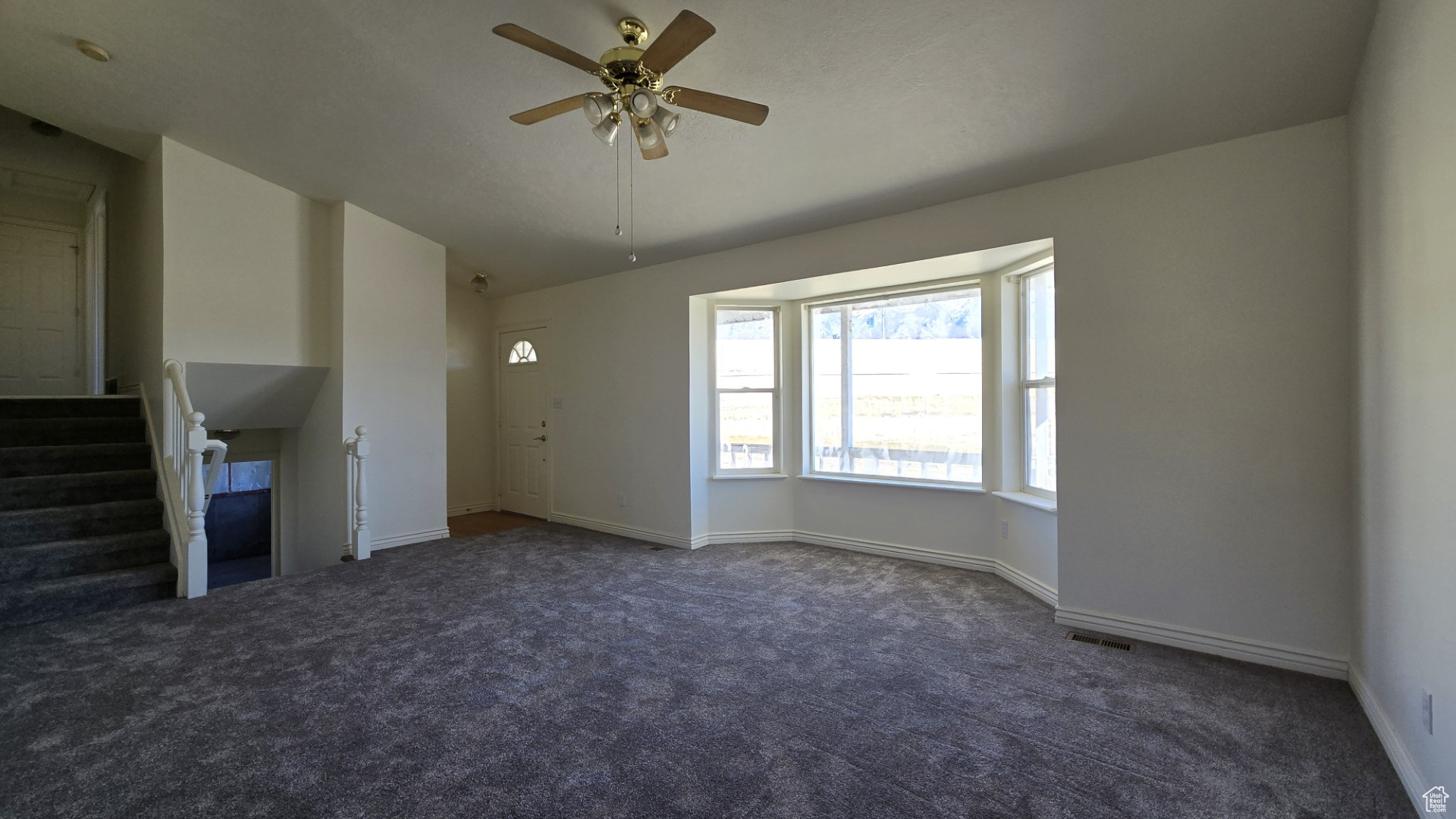 Unfurnished living room with visible vents, carpet flooring, baseboards, ceiling fan, and stairs