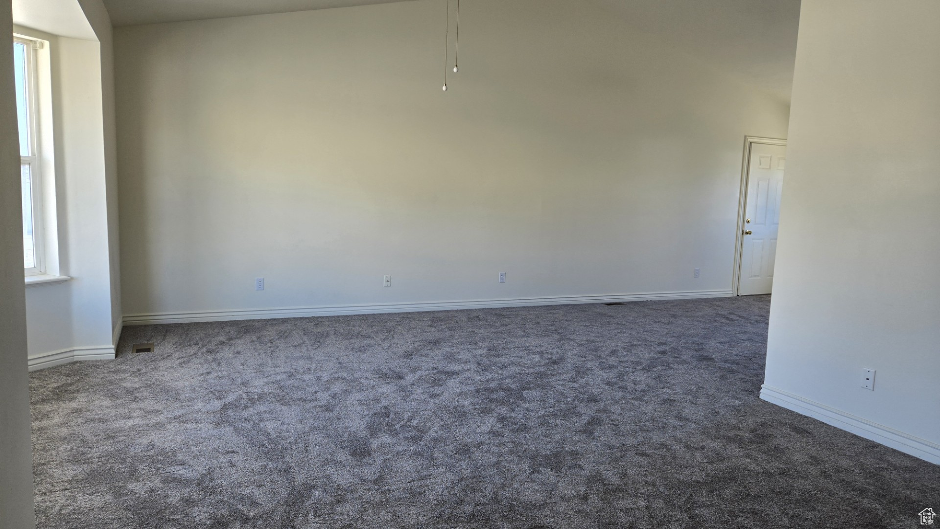 Carpeted empty room featuring baseboards and a high ceiling