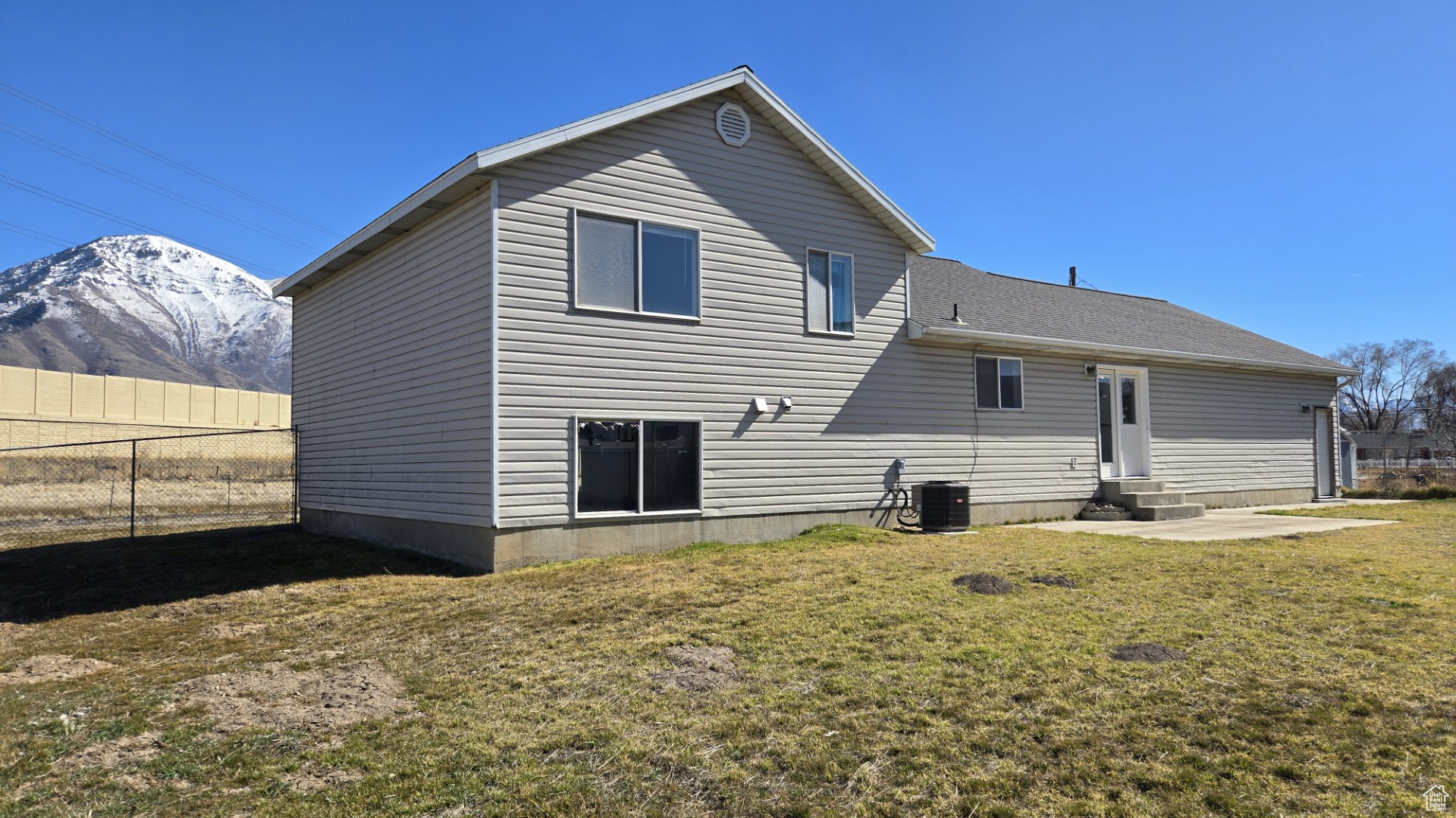 Rear view of property featuring fence, central air condition unit, entry steps, a lawn, and a mountain view