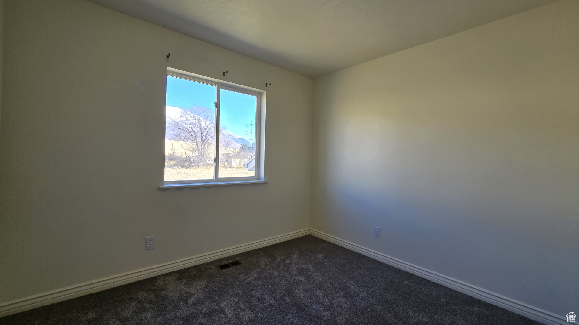 Spare room featuring visible vents, baseboards, and dark carpet