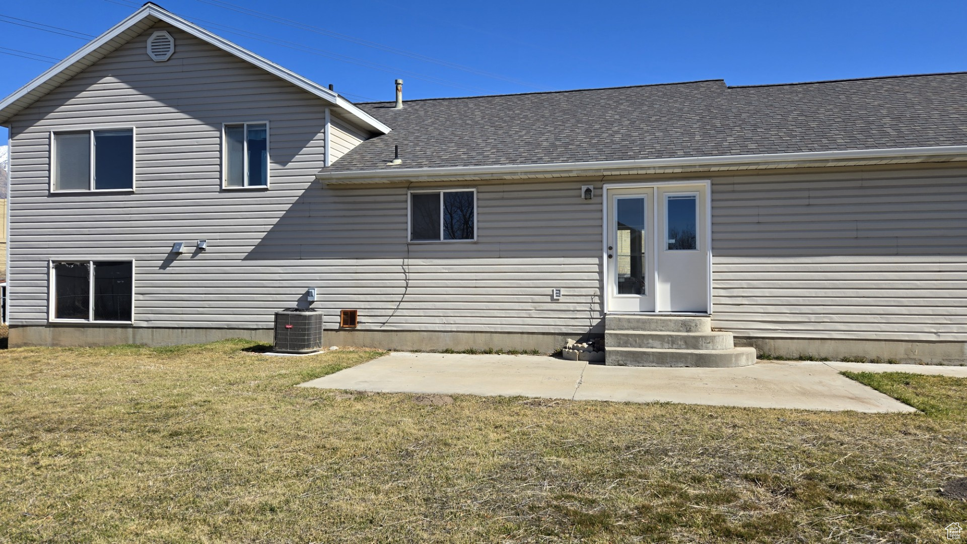 Back of property featuring a shingled roof, central air condition unit, entry steps, a yard, and a patio