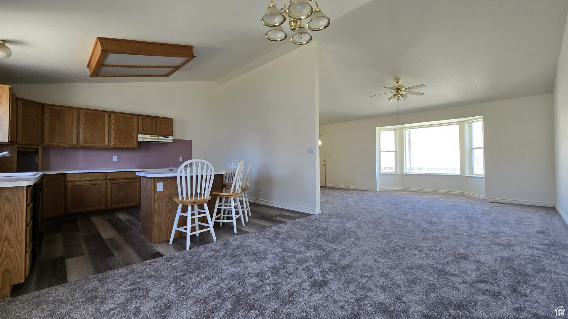 Kitchen with a breakfast bar, lofted ceiling, under cabinet range hood, brown cabinets, and dark carpet