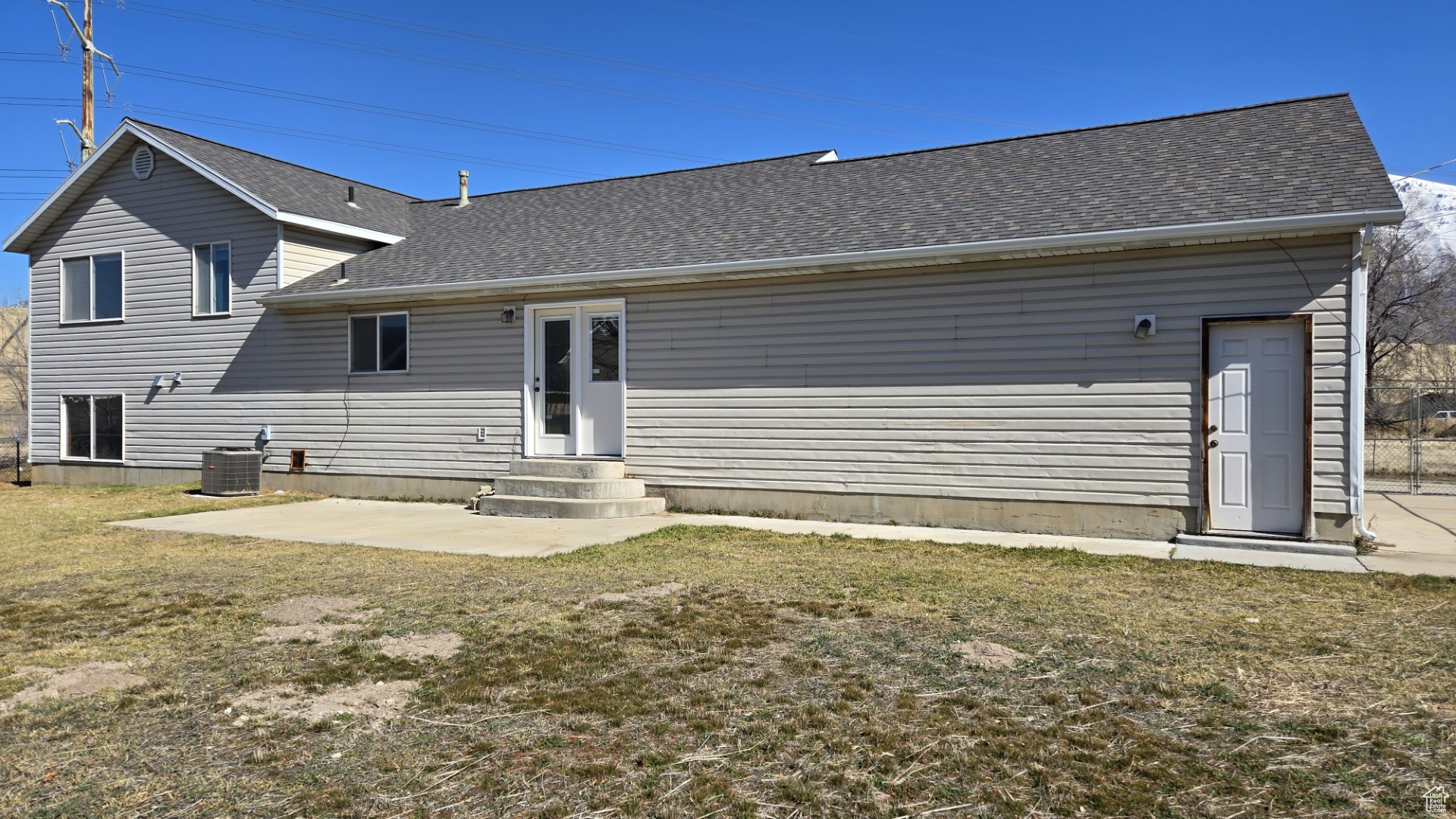 Back of house with cooling unit, a yard, roof with shingles, and entry steps