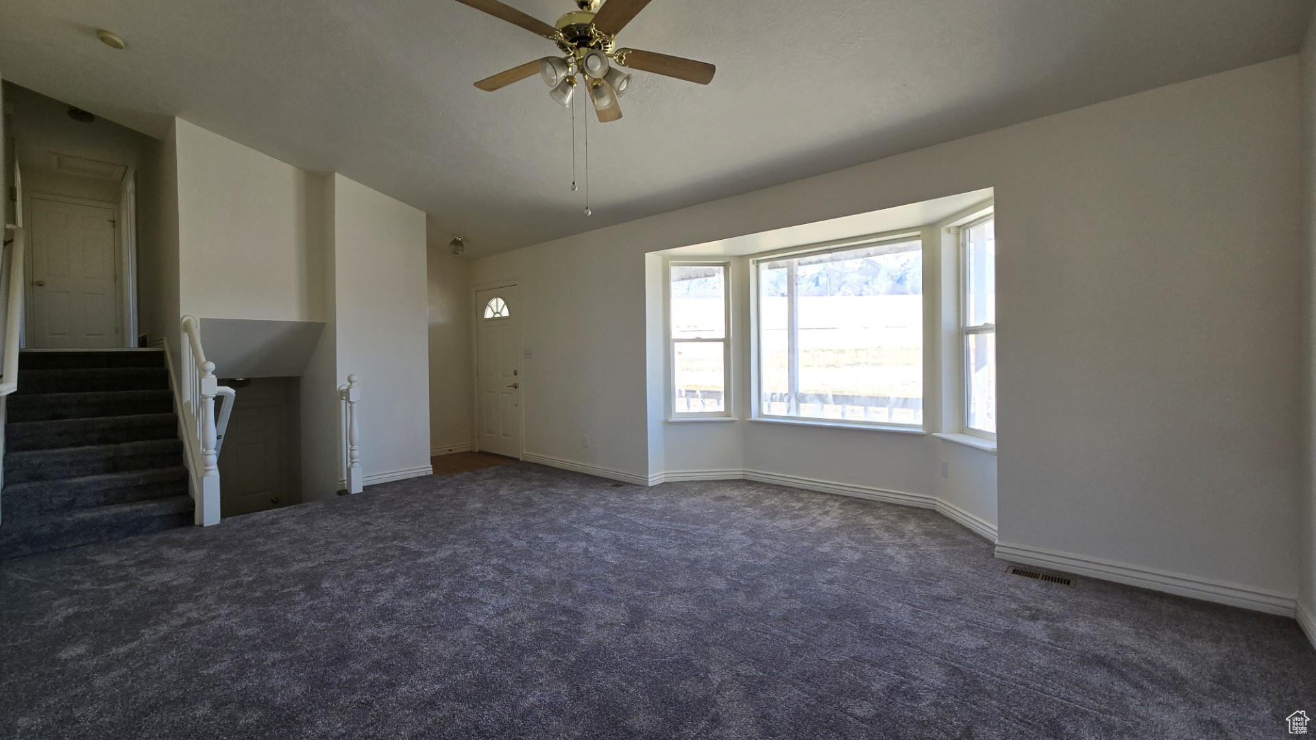 Unfurnished living room featuring visible vents, carpet flooring, baseboards, ceiling fan, and stairs