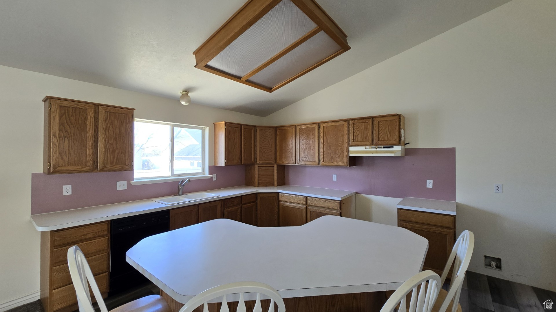 Kitchen featuring under cabinet range hood, lofted ceiling, black dishwasher, brown cabinetry, and a sink