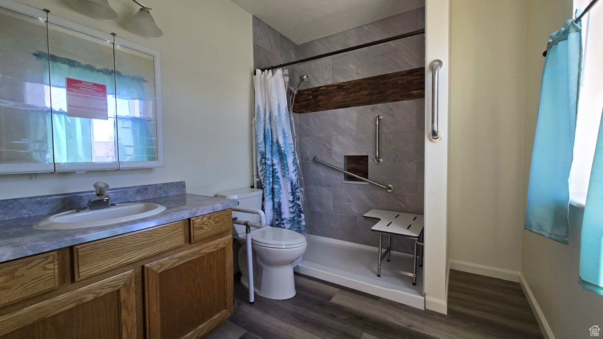 Bathroom featuring toilet, wood finished floors, a tile shower, baseboards, and vanity